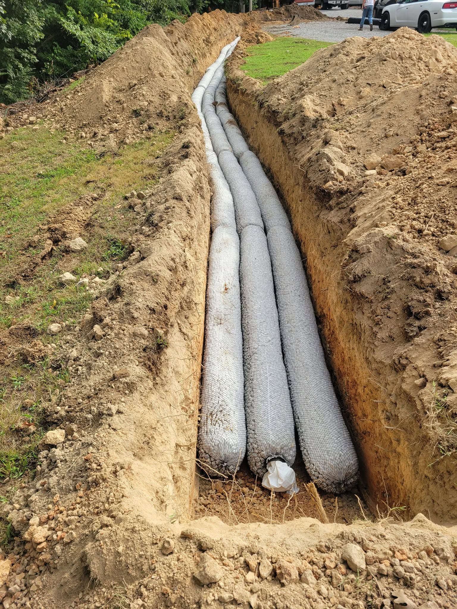 Three gray drainage pipes laid in a trench at a roadside construction site