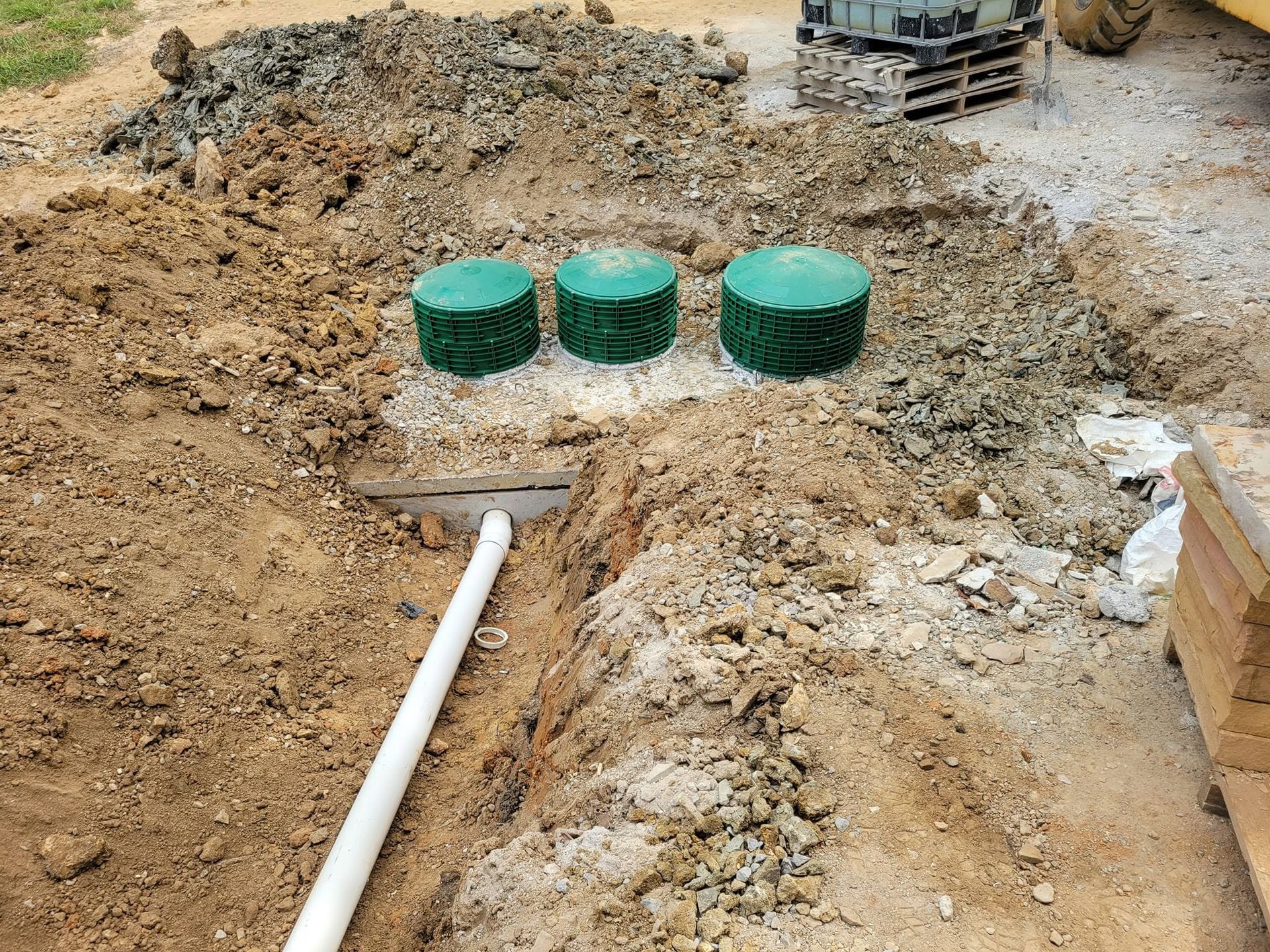Construction site with three green utility covers in a dirt trench beside a white pipe