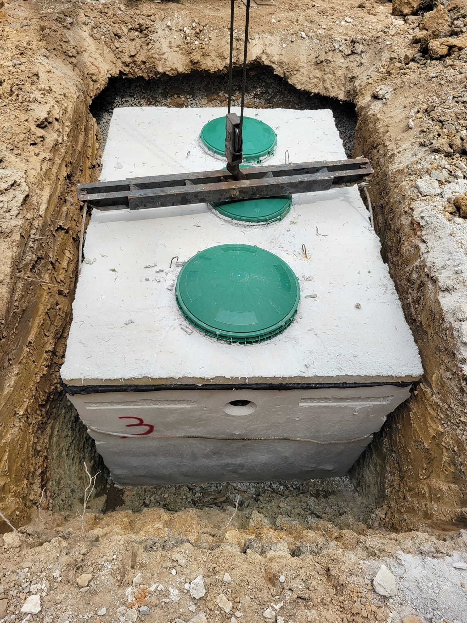 Concrete utility box in a dirt trench with two green circular caps and a cable across the top