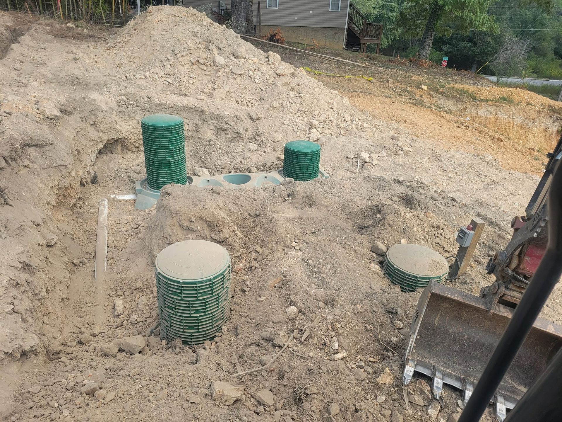 Construction site with dirt mound and green utility access lids near excavator bucket