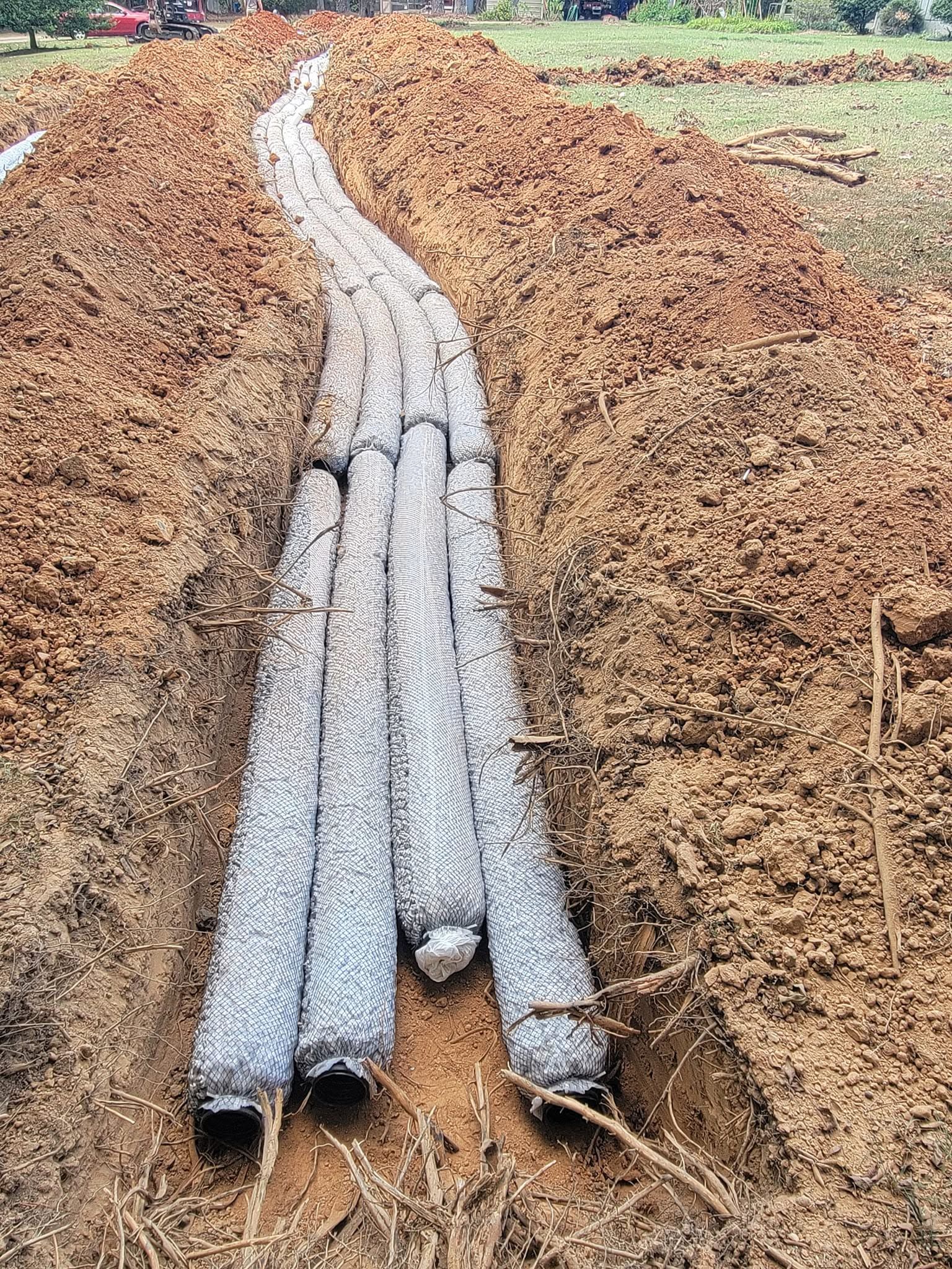 Bundle of white PVC pipes laid in a trench filled with brown soil outdoors.