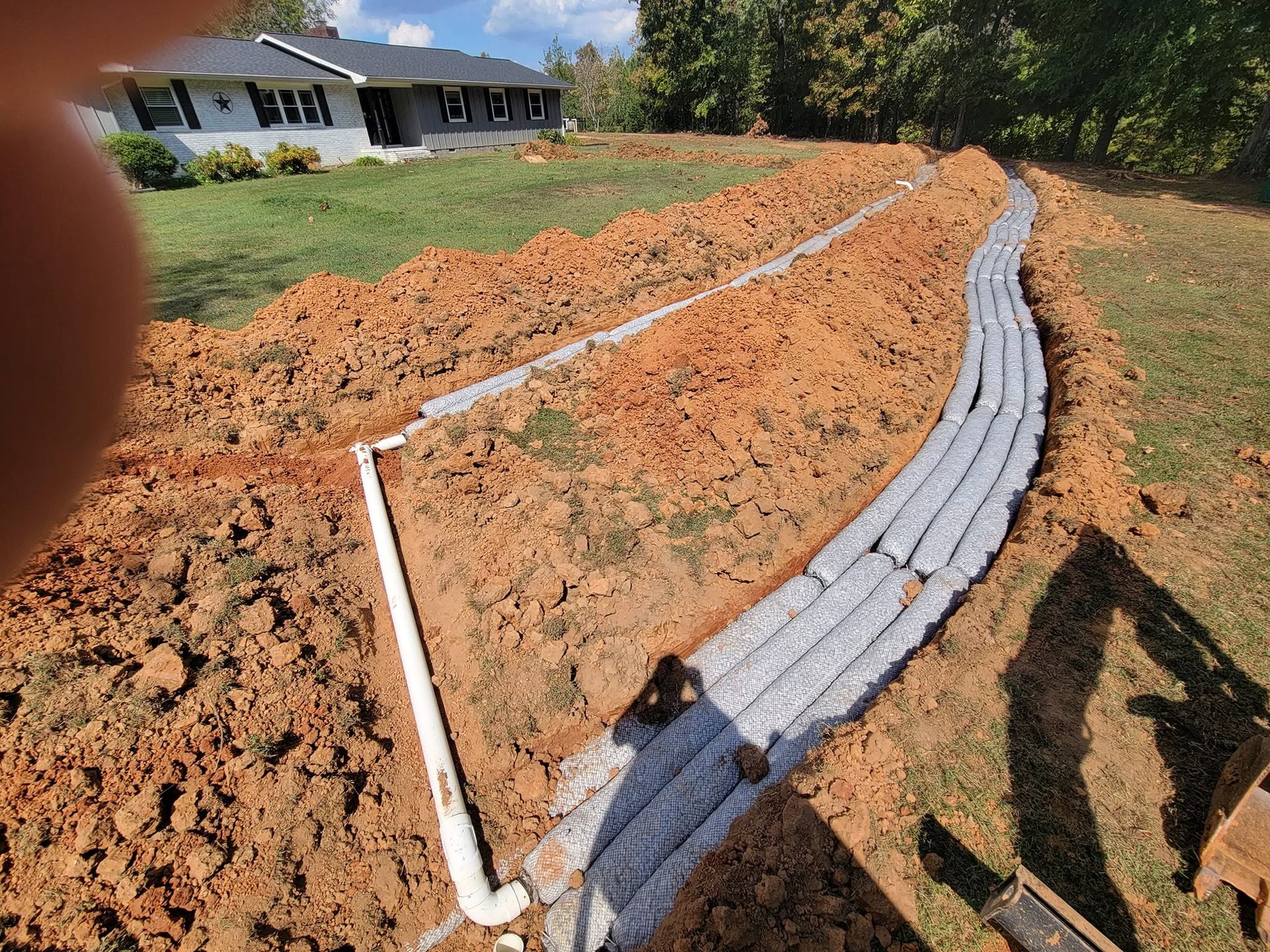 Construction site with a curved white drainage pipe and gray pavers in a dirt yard near a house.