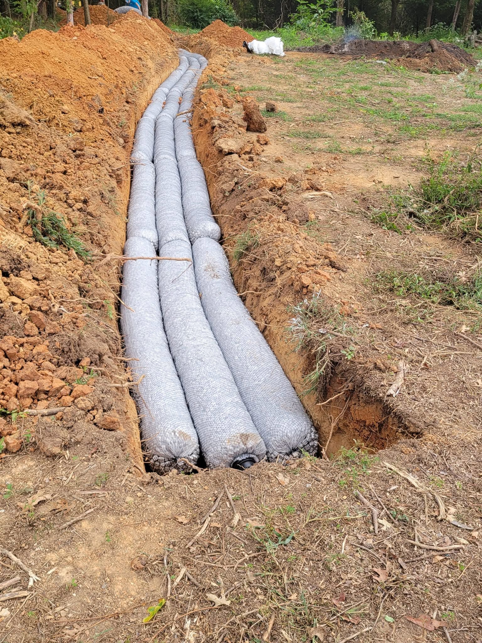 Four gray drainage pipes laid in a trench through a grassy dirt field