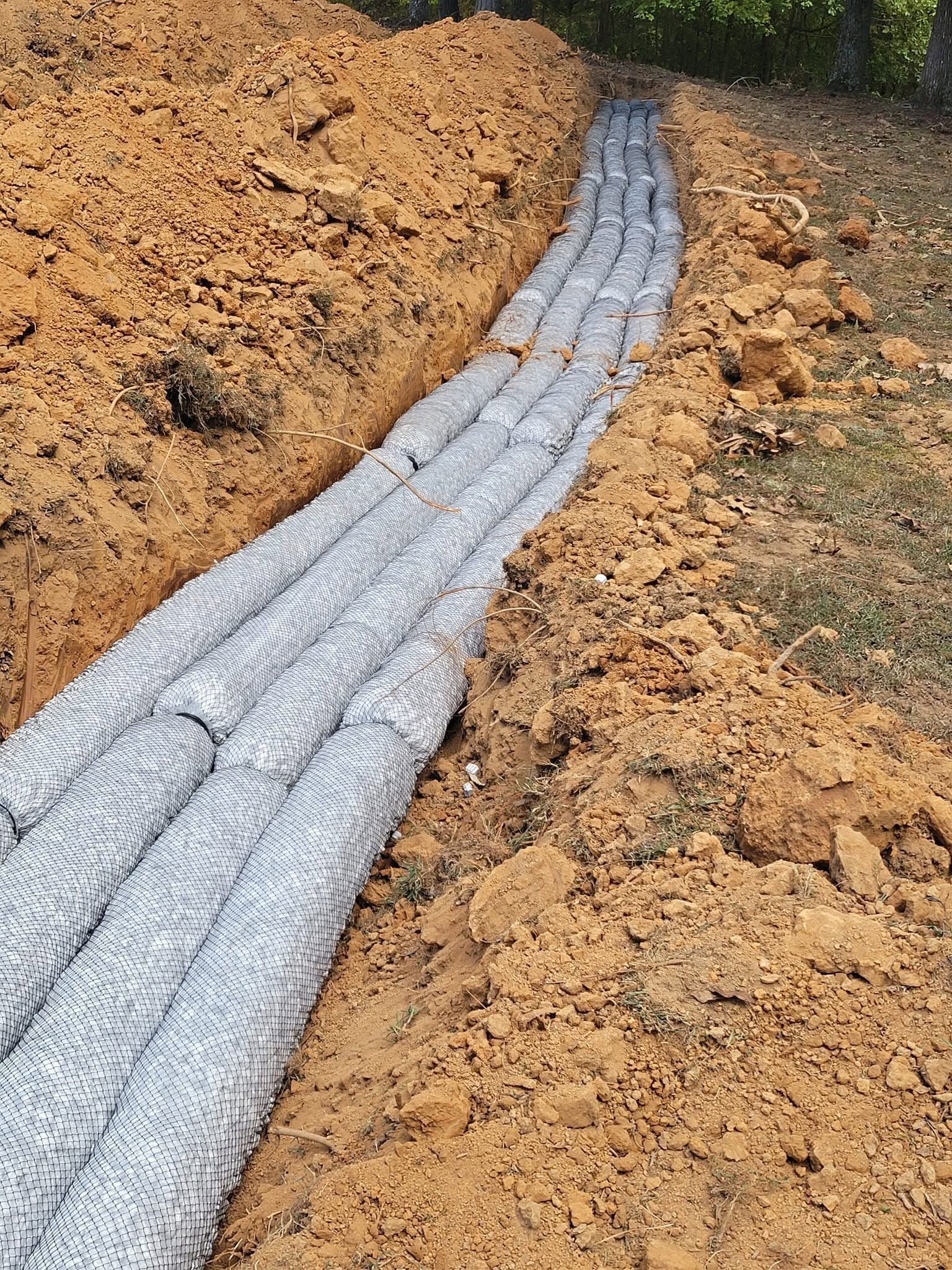 Gray pipe laid in a dirt trench, surrounded by loose soil and gravel.