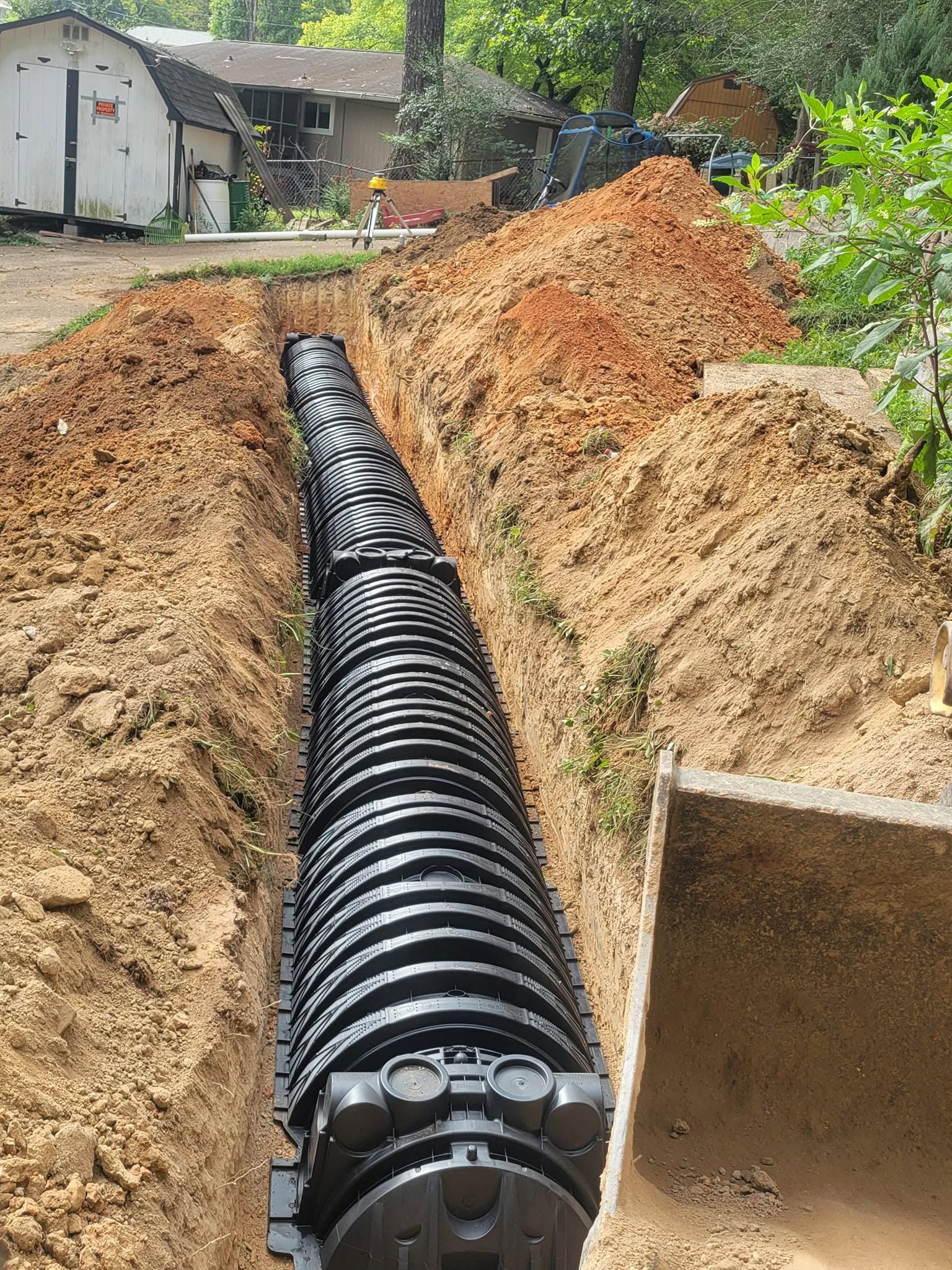 Black corrugated drainage pipe laid in a dirt trench at a construction site