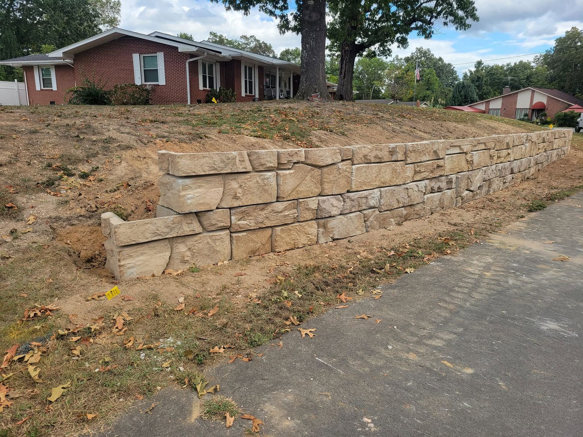 Stone retaining wall beside a suburban house on a sloped yard, next to a paved street