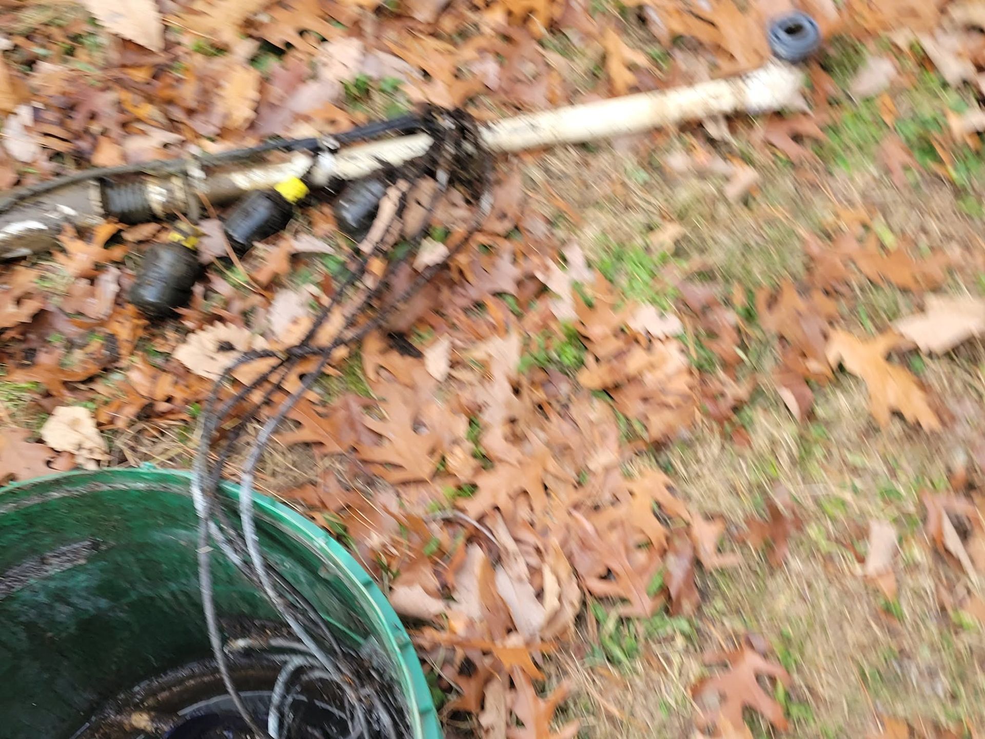 Fishing rod and gear on fallen leaves beside a green bucket outdoors