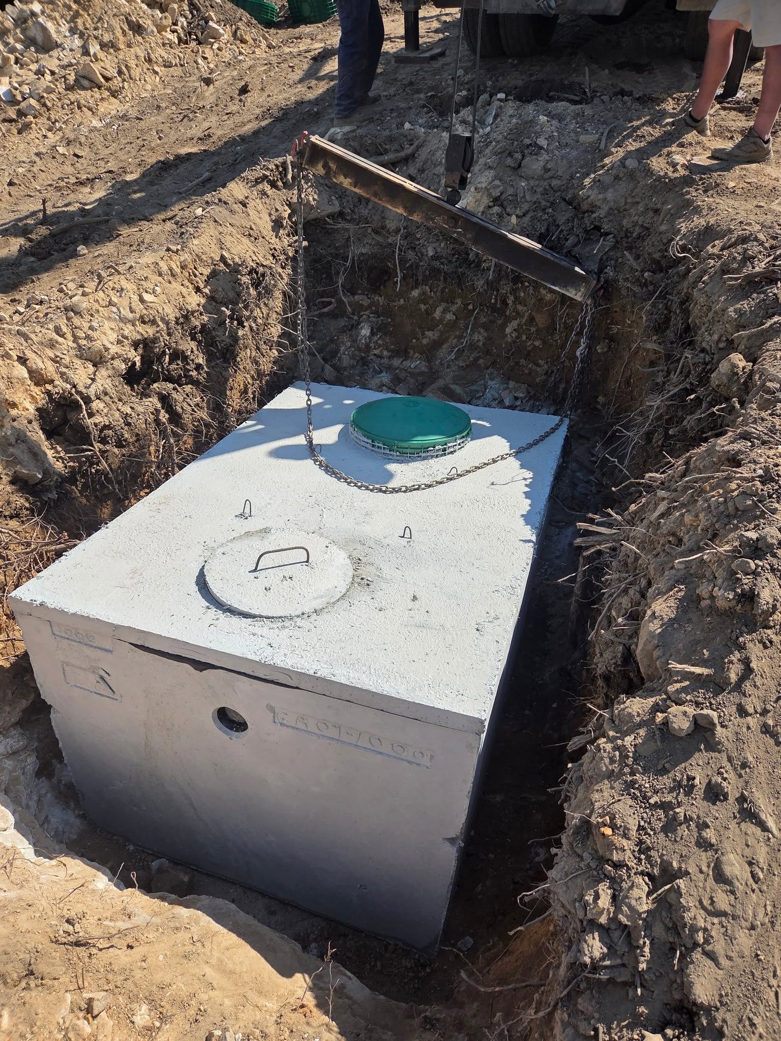 Concrete underground utility tank in a dirt trench with a green cap and circular access cover.