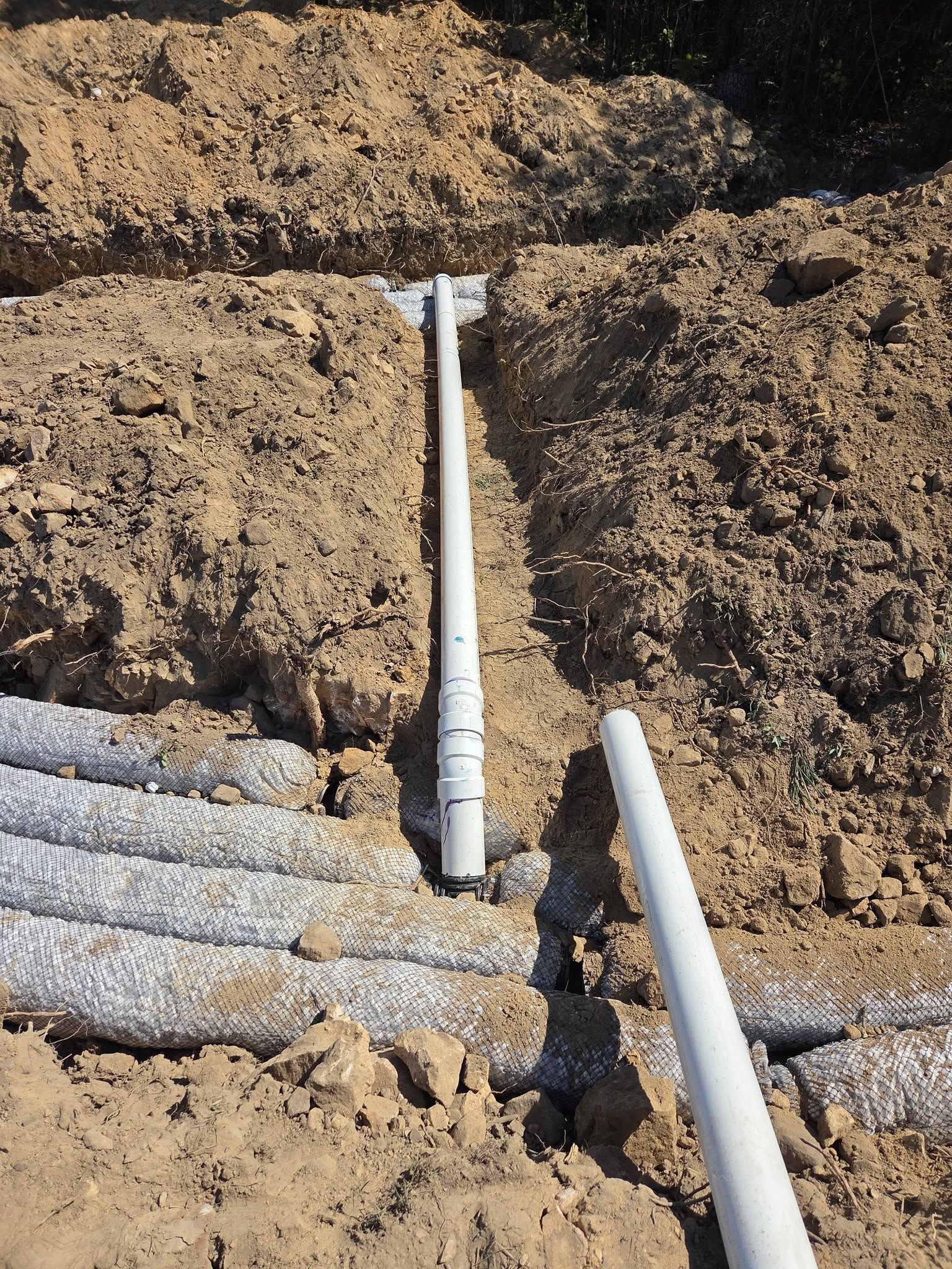 White PVC pipes laid in a dirt trench at a construction site