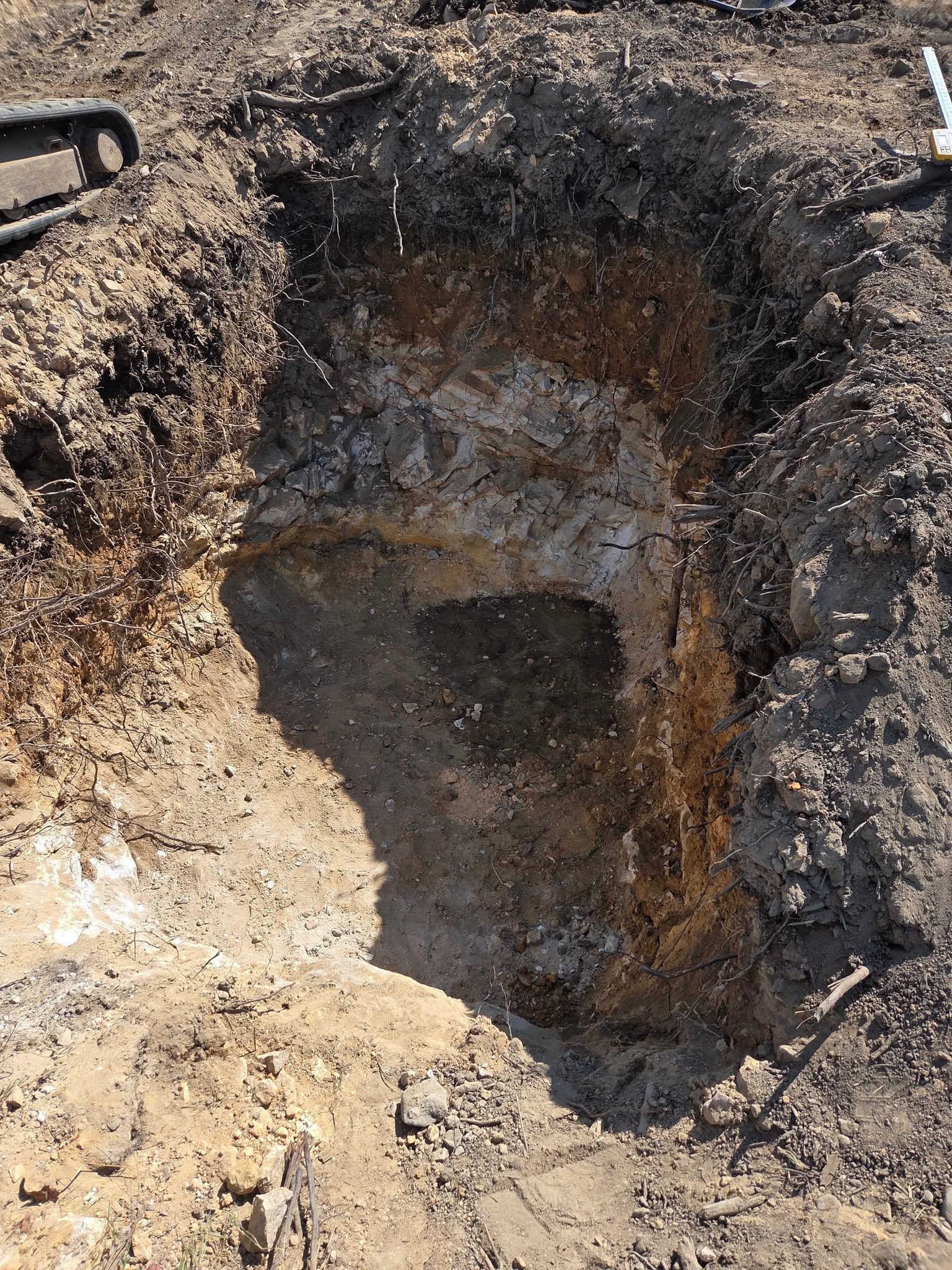 A deep excavation hole in rocky soil with rough dirt walls and a dark, uneven bottom.