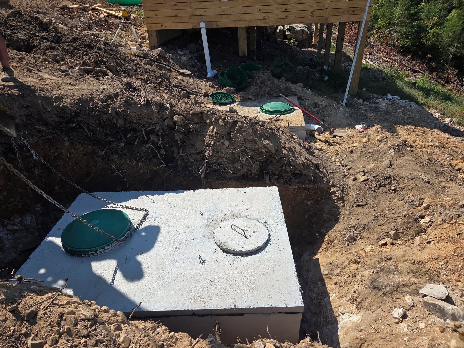 Concrete septic tank cover with two green lids in a dug-out dirt area outdoors