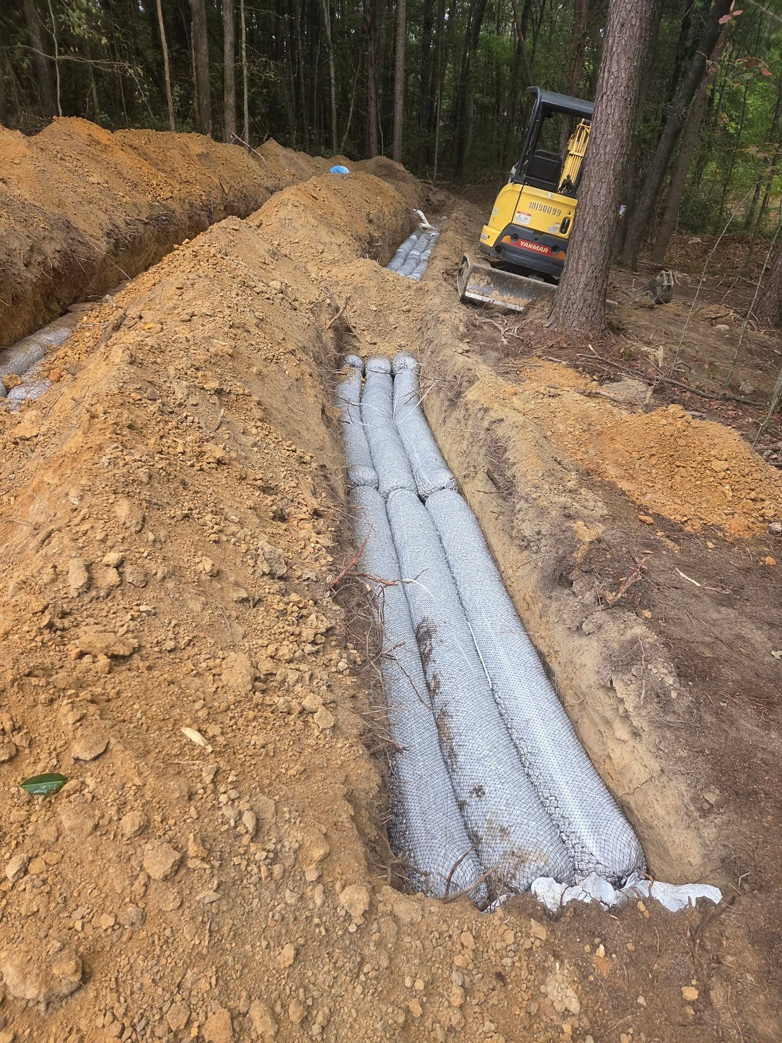 Excavator beside a long trench filled with wet concrete in a wooded construction site