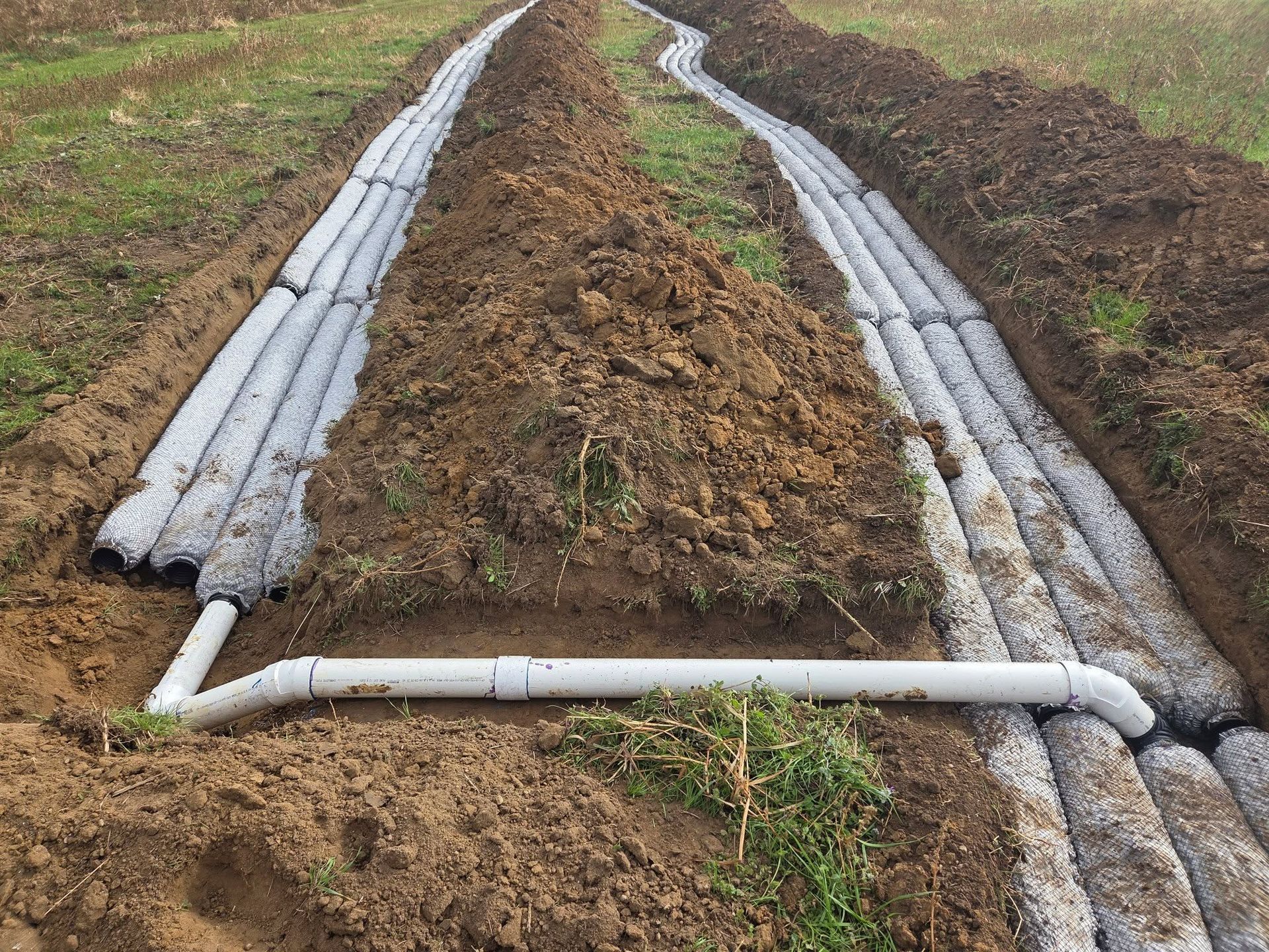 Irrigation pipes running along plowed field rows, with a white crosspipe in the foreground.