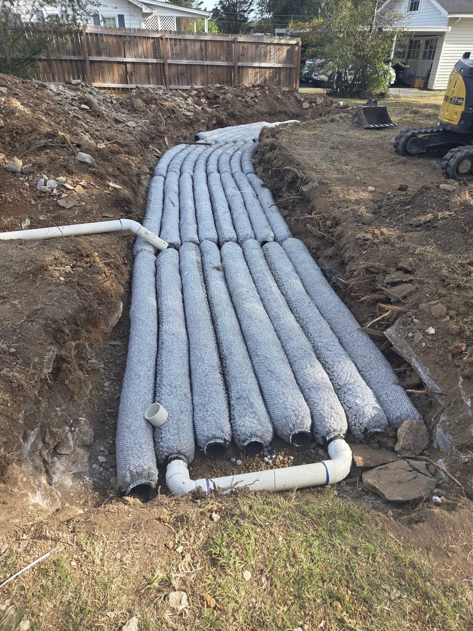 Gray drainage pipes laid in a trench between excavated soil, forming a curved underground utility line.