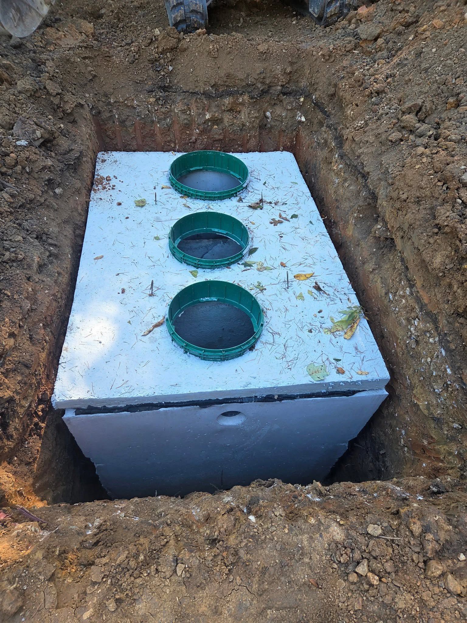 White utility box in a dirt trench with three green pipe openings on top.