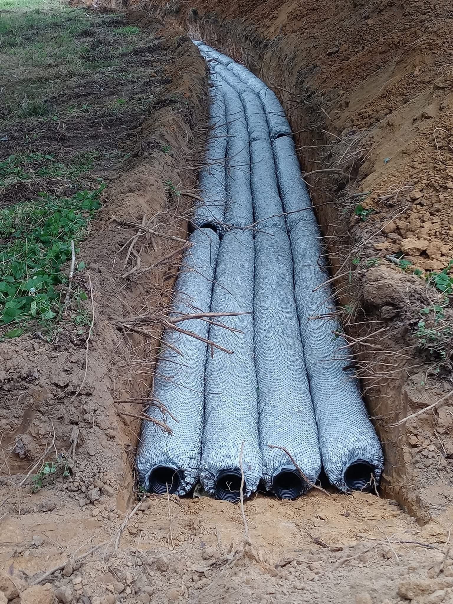 Gray pipes laid in a dirt trench along a hillside, stacked in a row.