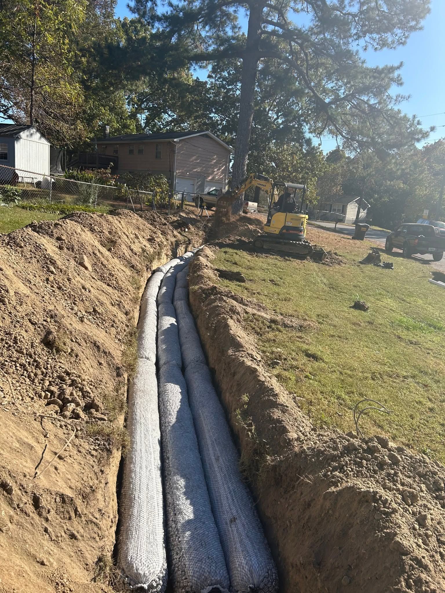 Trenched hillside with black drainage pipe and white insulation lining a grassy yard near houses