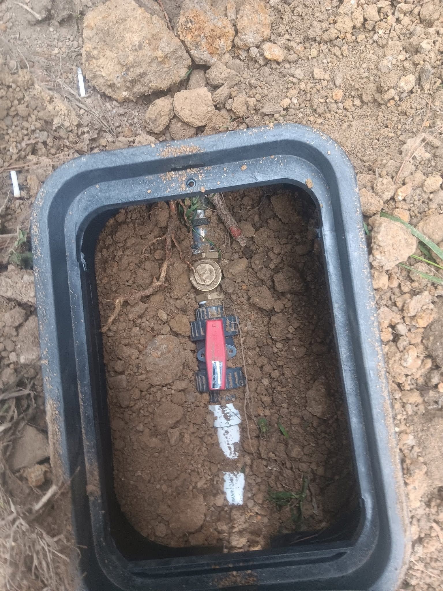 Open utility box with exposed wires and a red valve in dirt, underground service access.