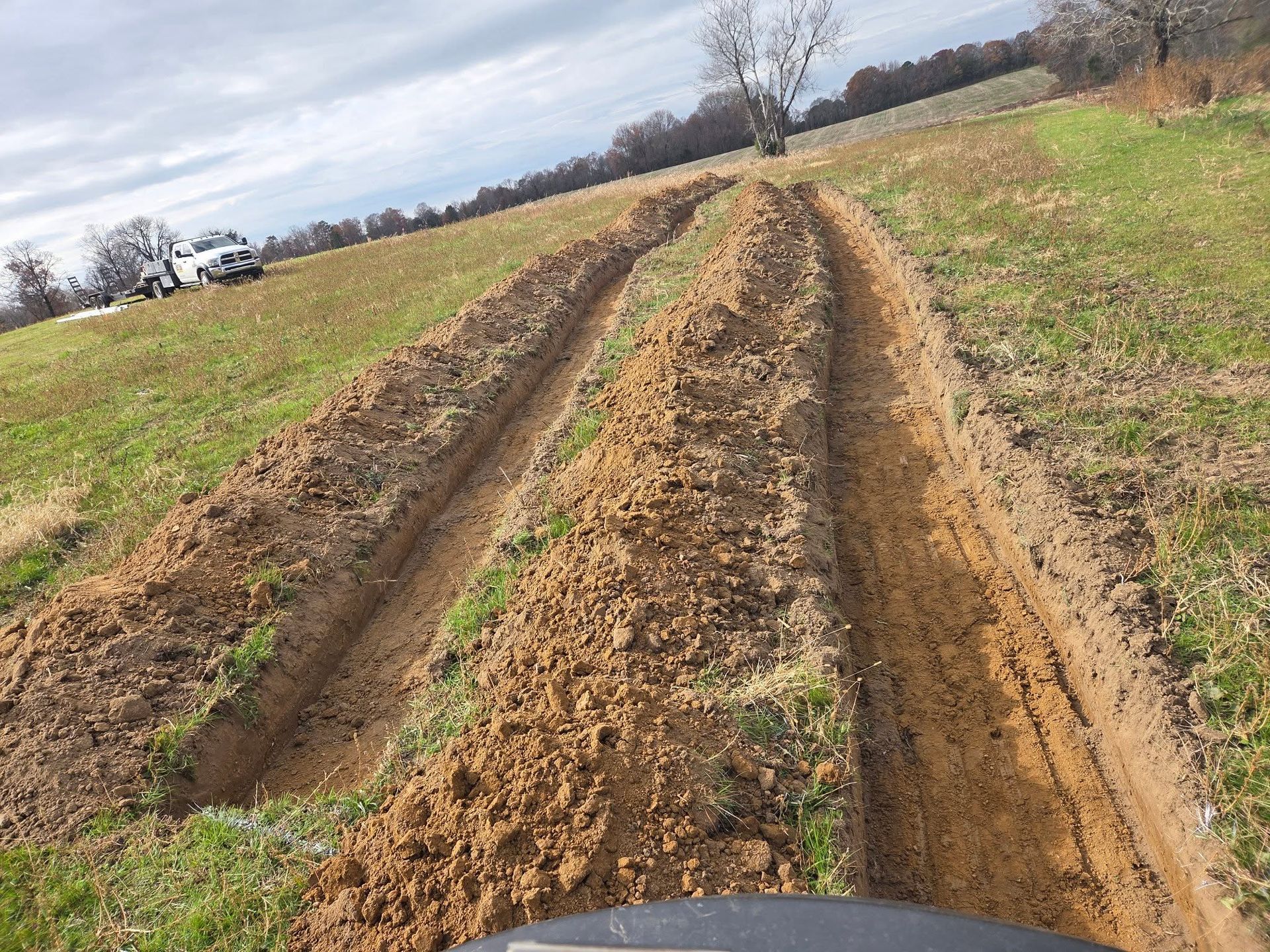 Fresh mud tracks cut through a grassy field under a cloudy sky.