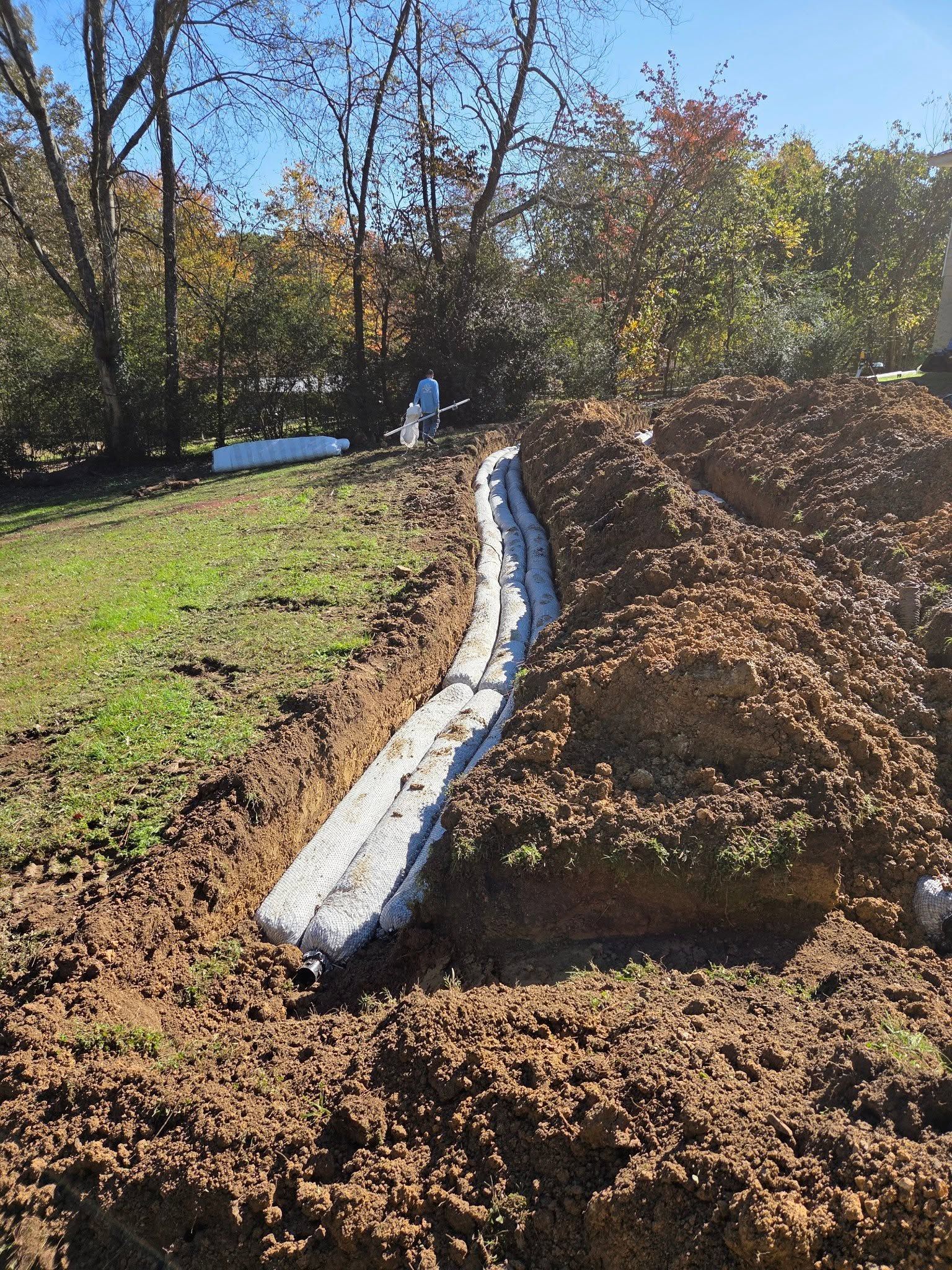 Long white drainage pipe running through a grassy dirt slope in a wooded yard
