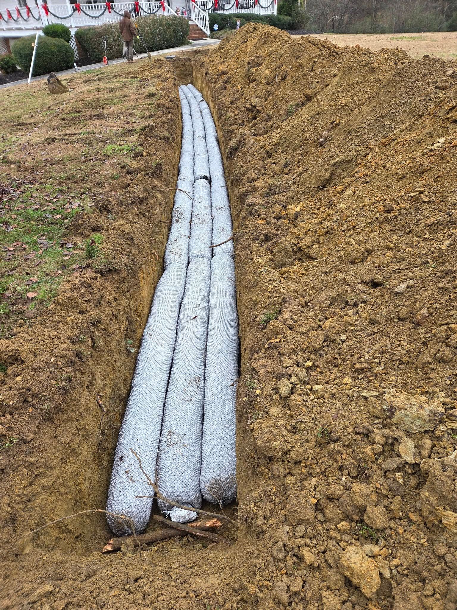Three silver pipes laid in a dirt trench beside a mound of soil outdoors