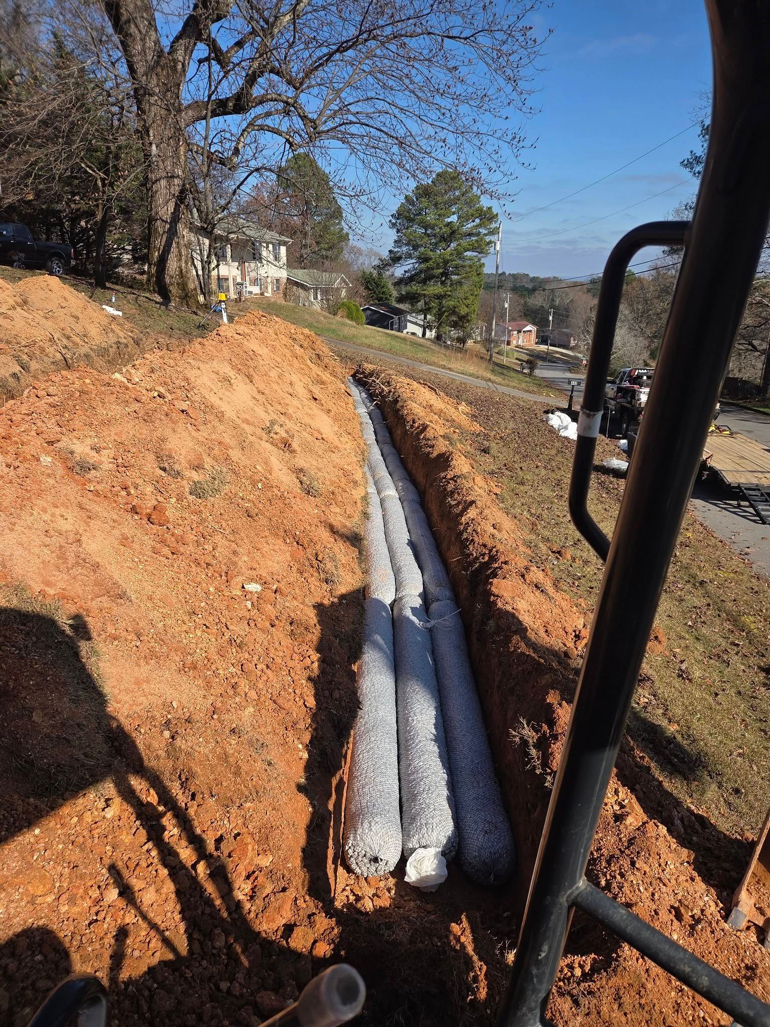 Two white pipes laid in an orange dirt trench on a sloped construction site.