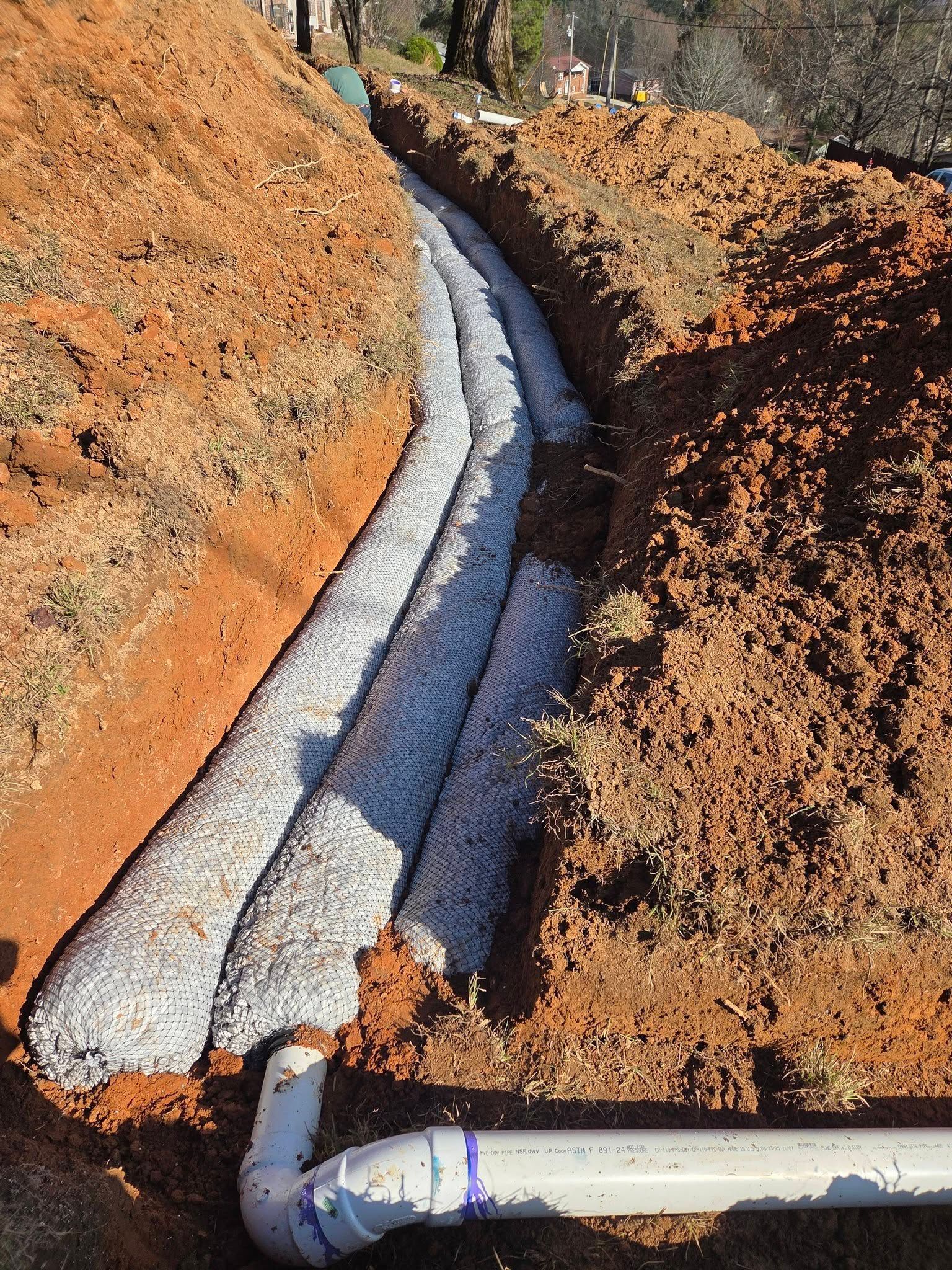 White insulated pipe running through a narrow trench in orange-brown soil outdoors
