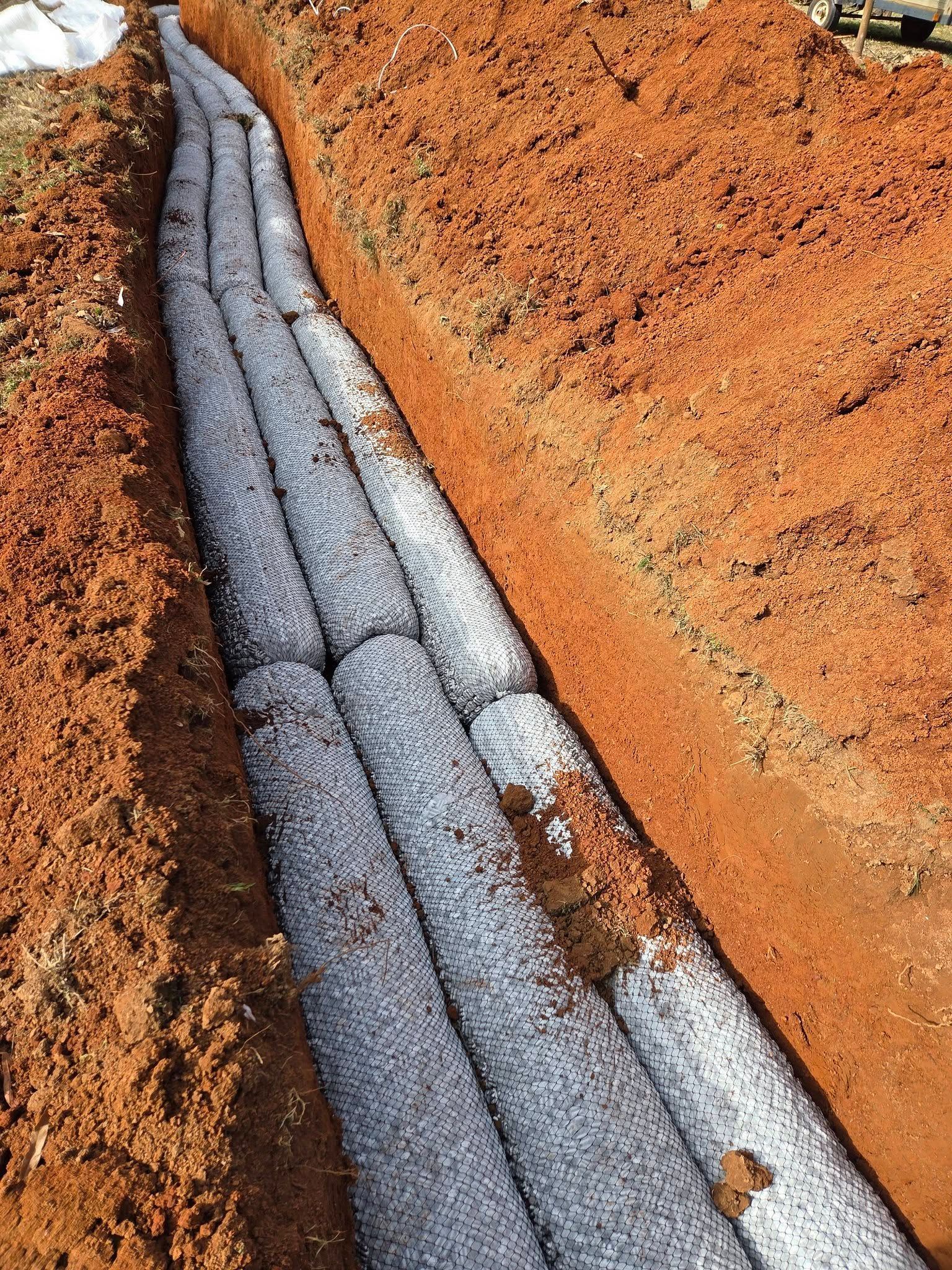 Gray drainage pipe in a dirt trench with orange soil on both sides