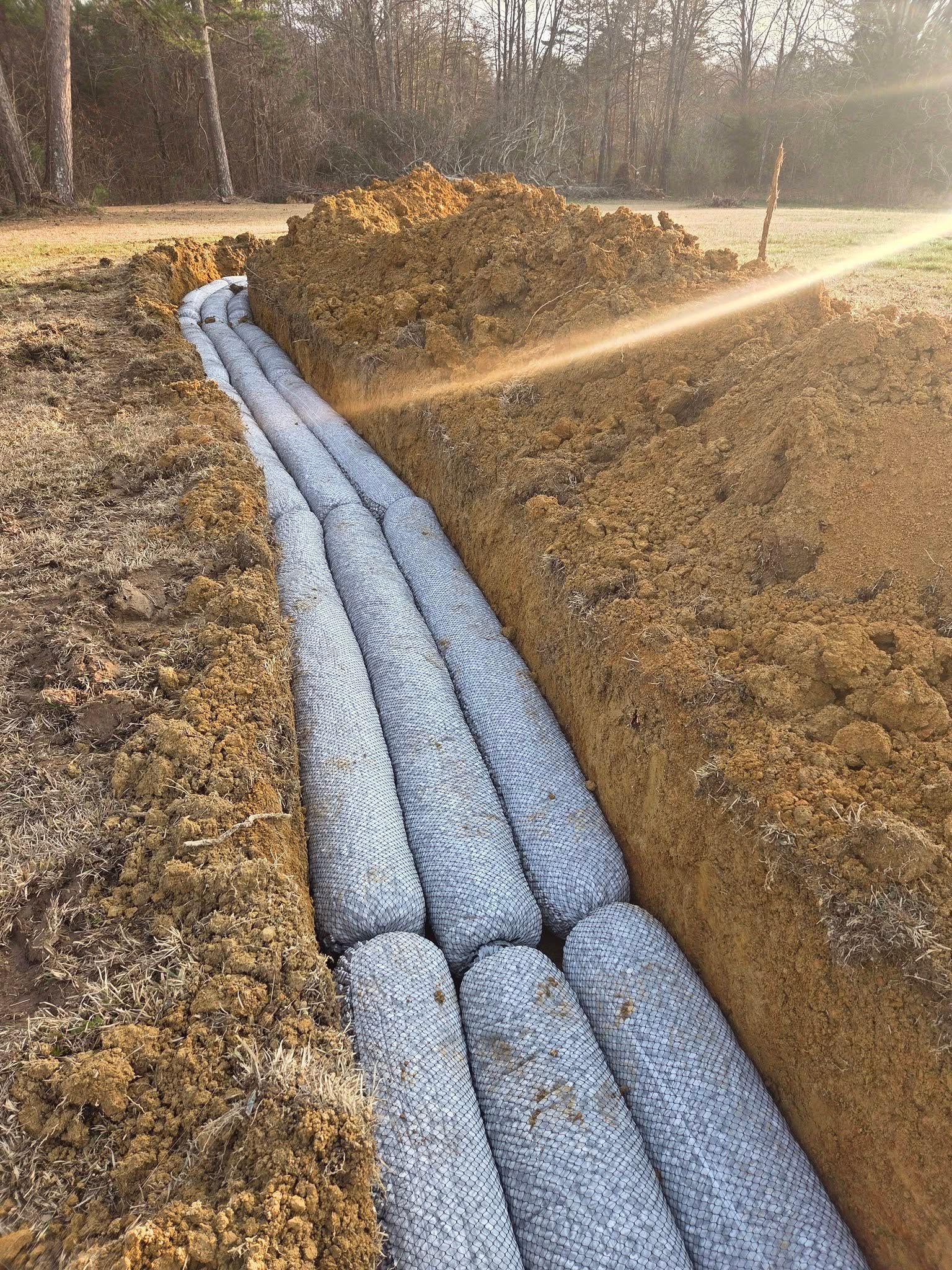 Installed drainage pipe in a trench at a construction site, surrounded by gravel and dirt.