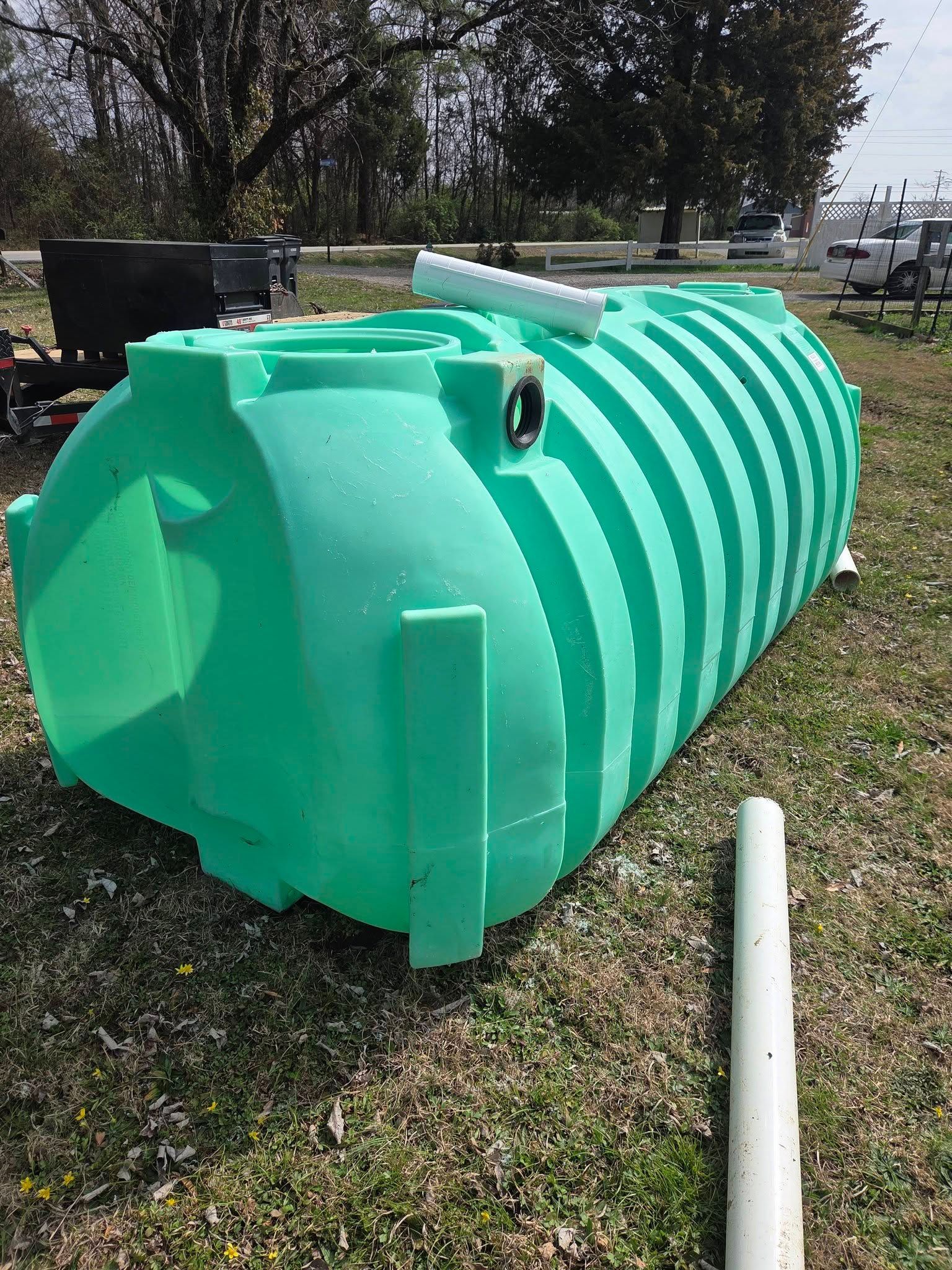 Large turquoise cylindrical tank on the ground outdoors, with ribbed sides and a white pipe nearby.