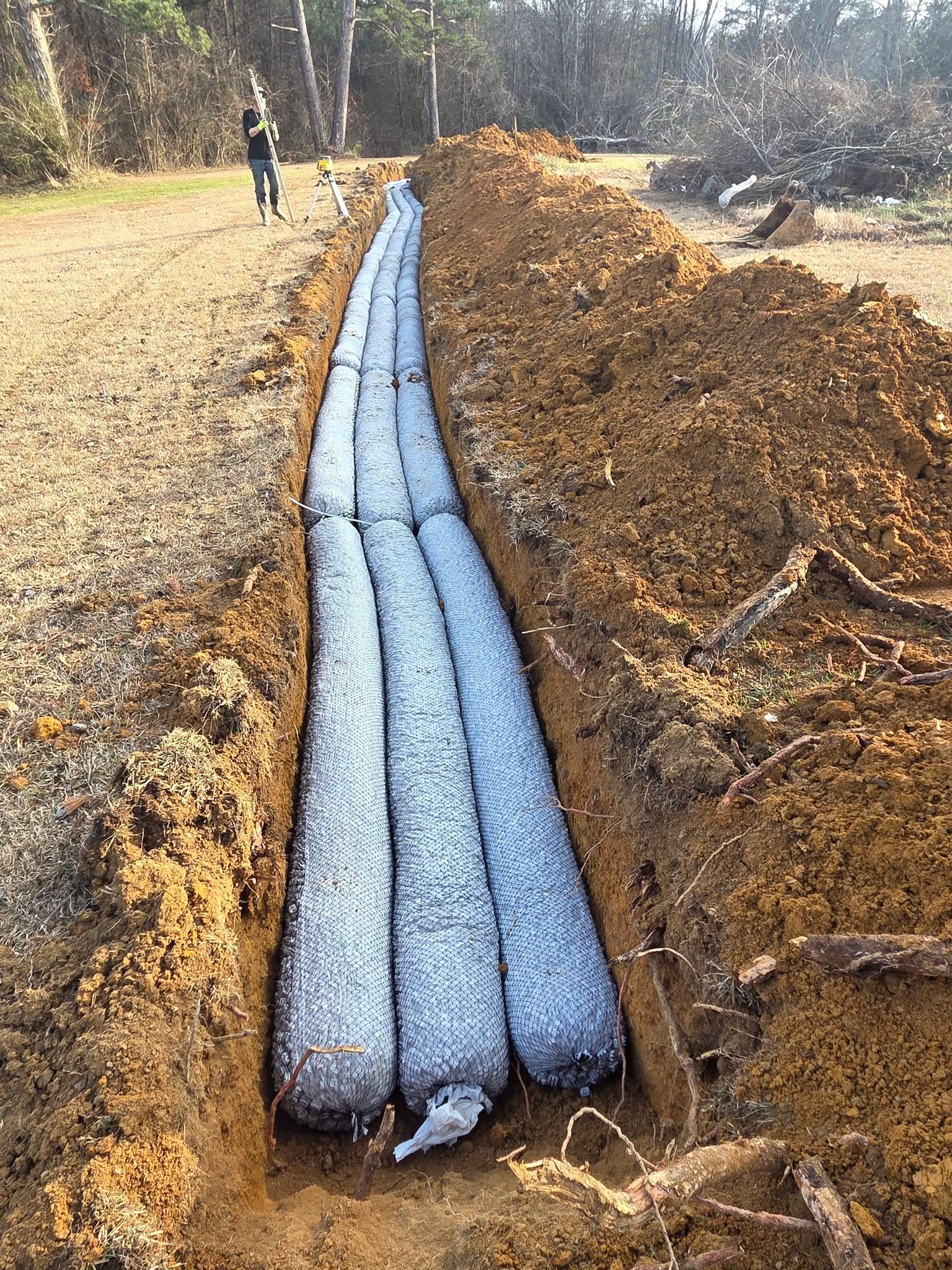 Blue drainage pipe laid in a dirt trench along a roadside, with soil piled on both sides.