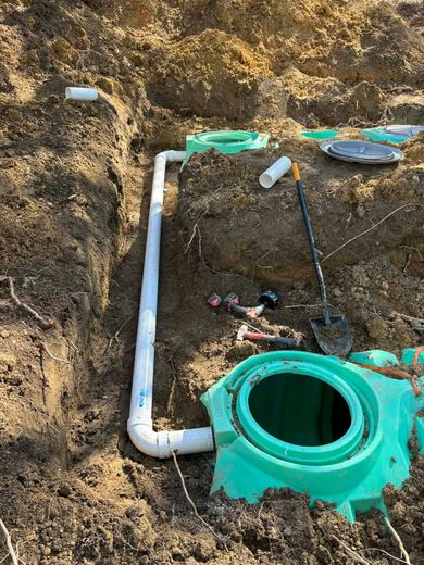 Underground plumbing trench with white PVC pipes and a green septic tank riser in soil