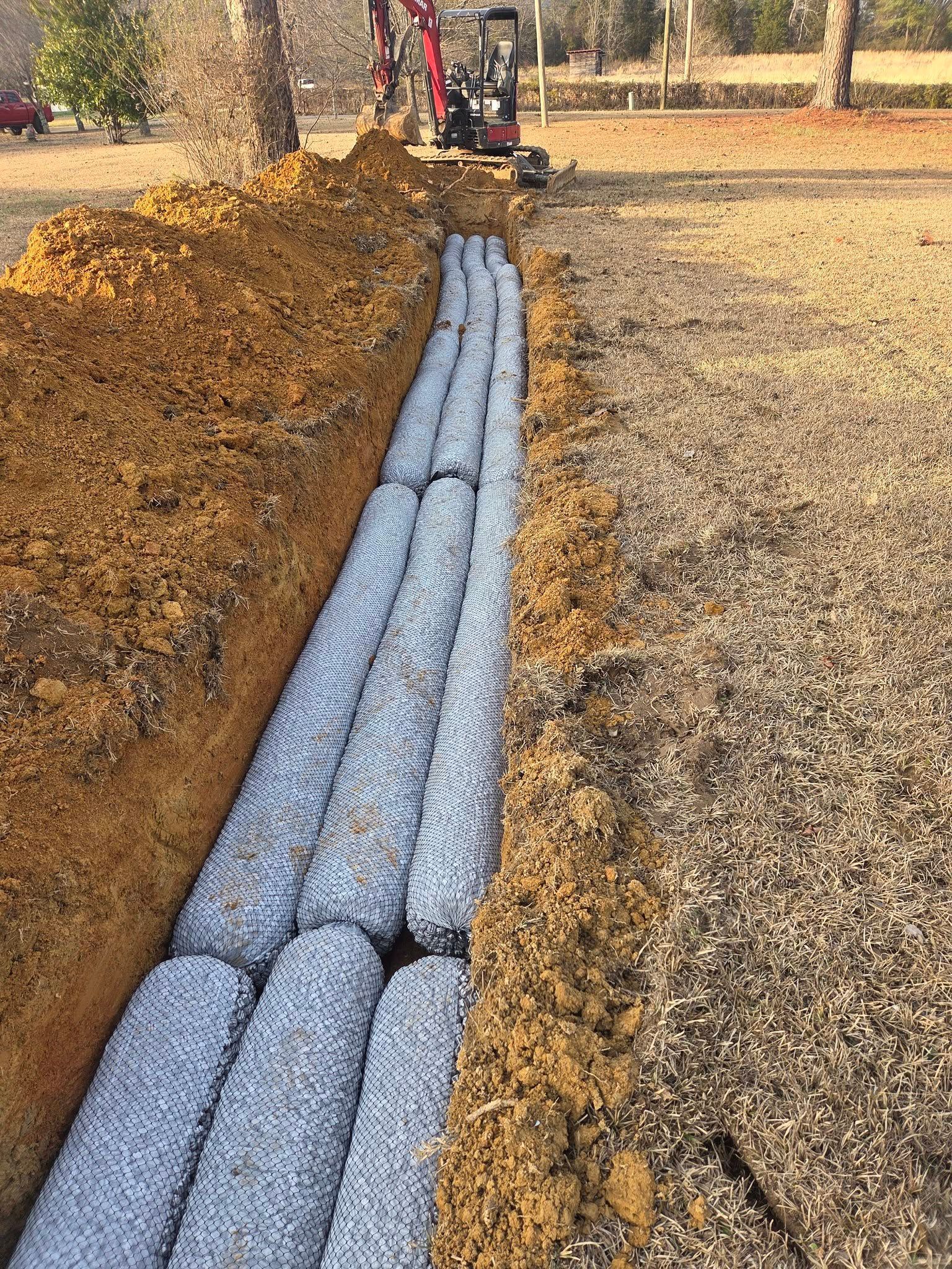 Blue pipes laid in a trench beside a dirt mound on a leaf-covered worksite.