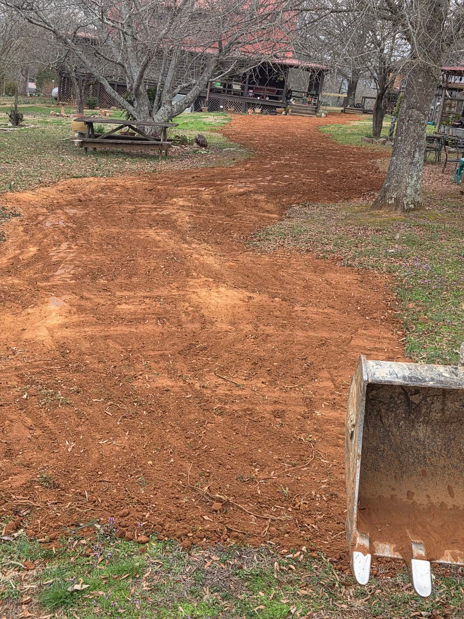Backyard path covered in orange mulch, with bare trees and a small concrete feature in the foreground