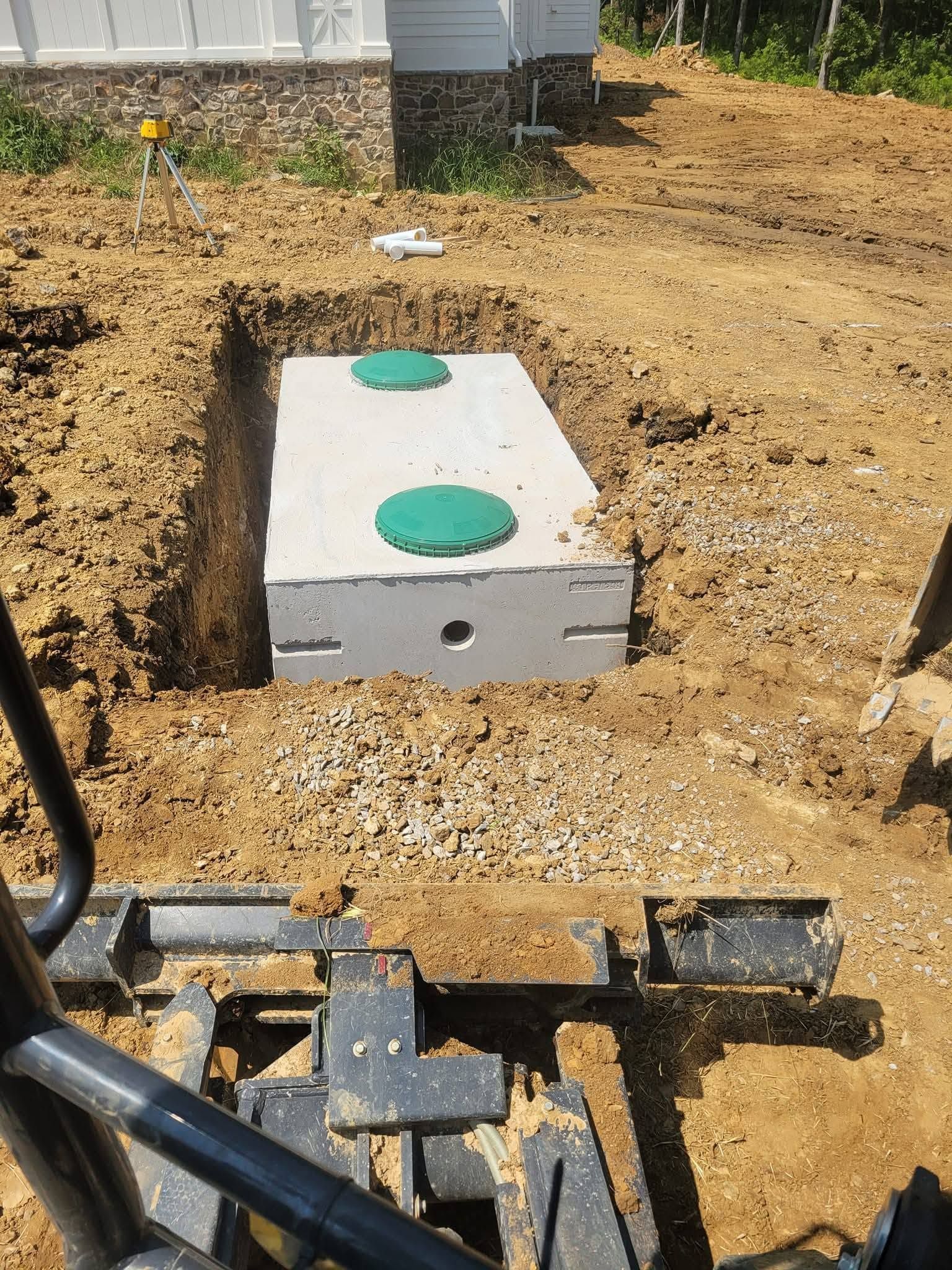 Rectangular utility box in a dirt excavation, with green lids on top and construction equipment nearby