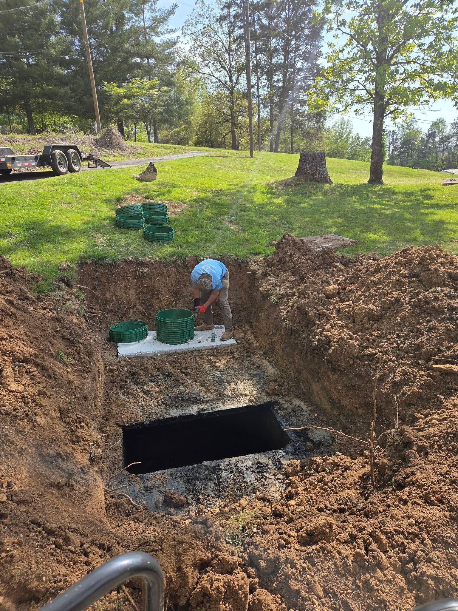 Worker inspecting an excavated concrete basement opening in a grassy yard