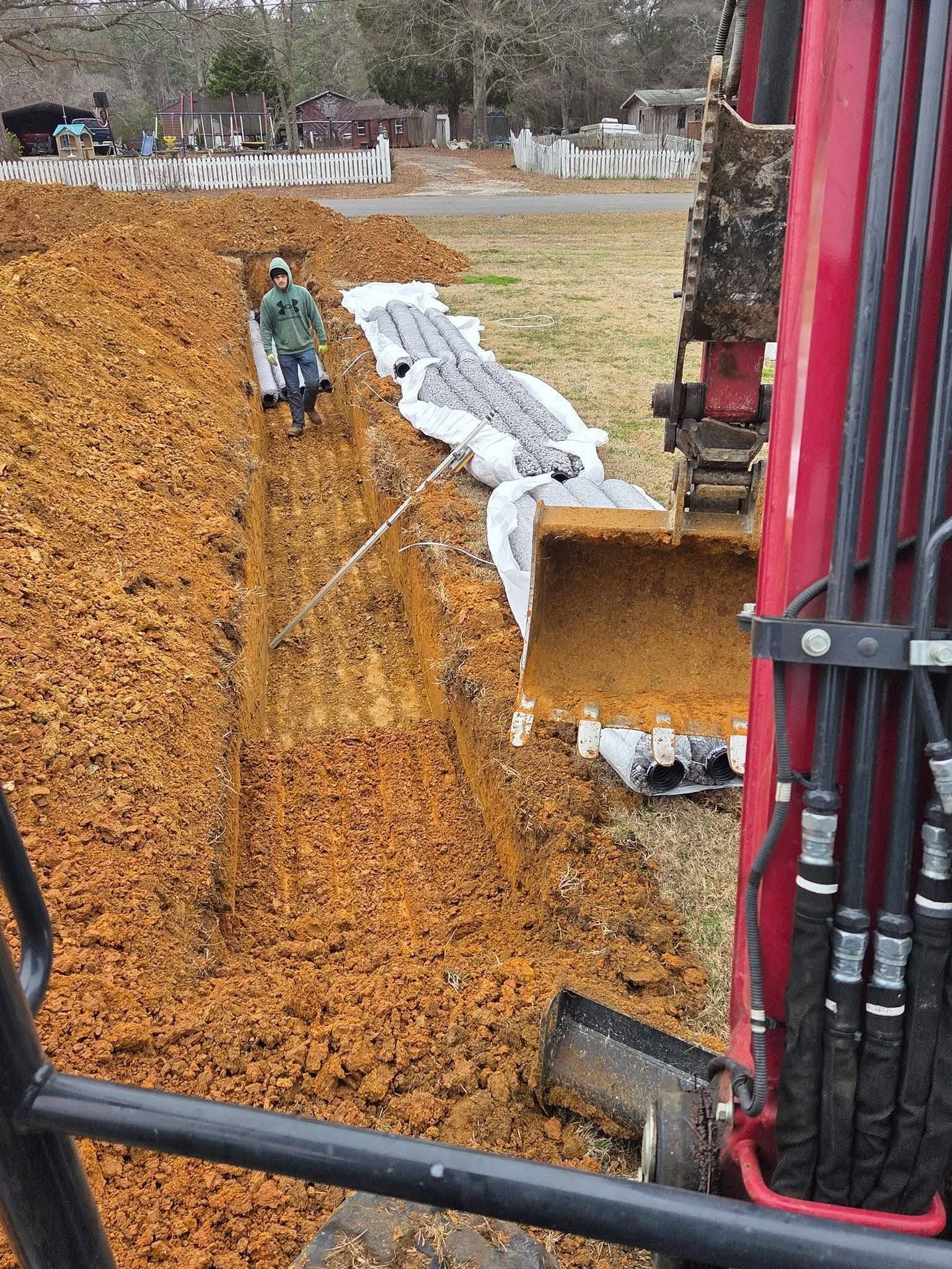 Worker on a sloped grain pile near a red conveyor, with white tarp-covered material beside the load area.