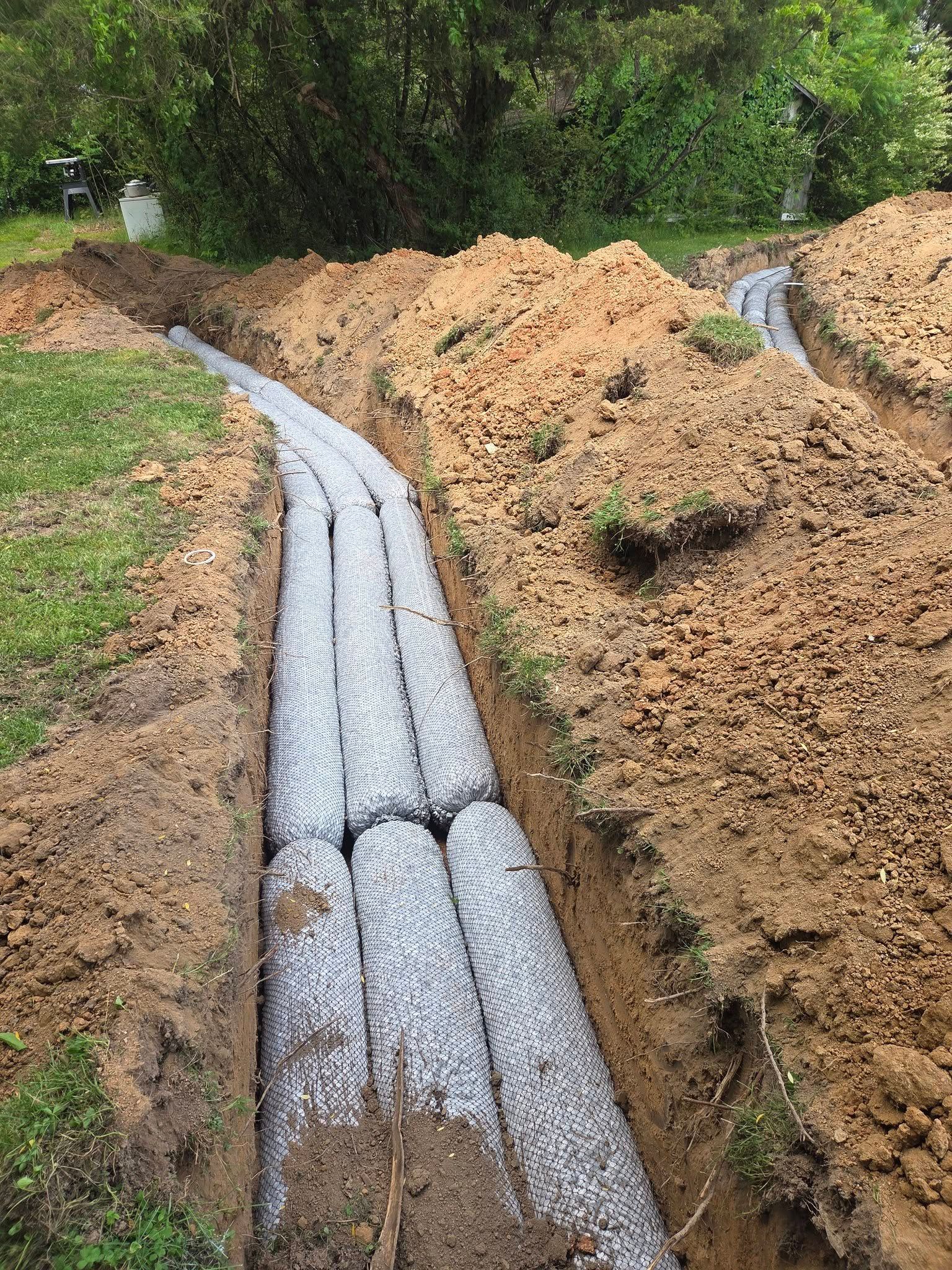 Plastic drainage pipes laid in a muddy trench alongside a grassy path and dirt embankment.