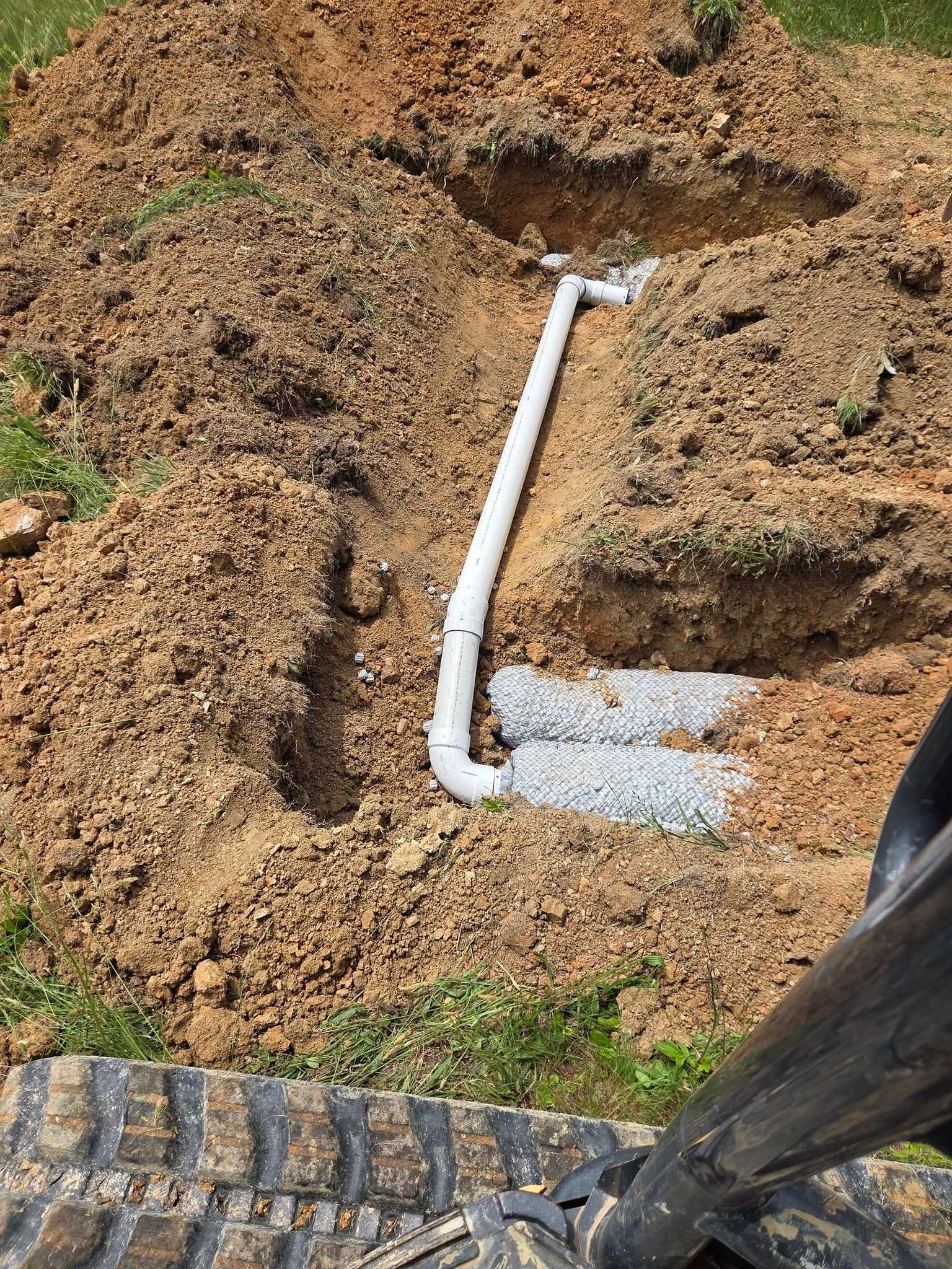 White PVC pipe trench in dirt beside a brick walkway