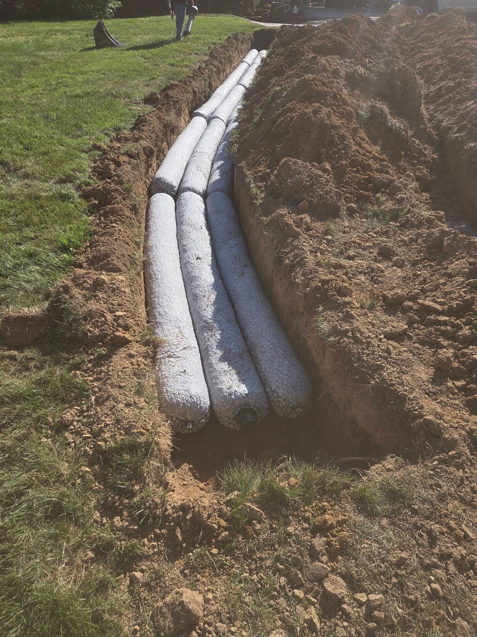 Sandbags lining a trench along a grassy field under bright sunlight.