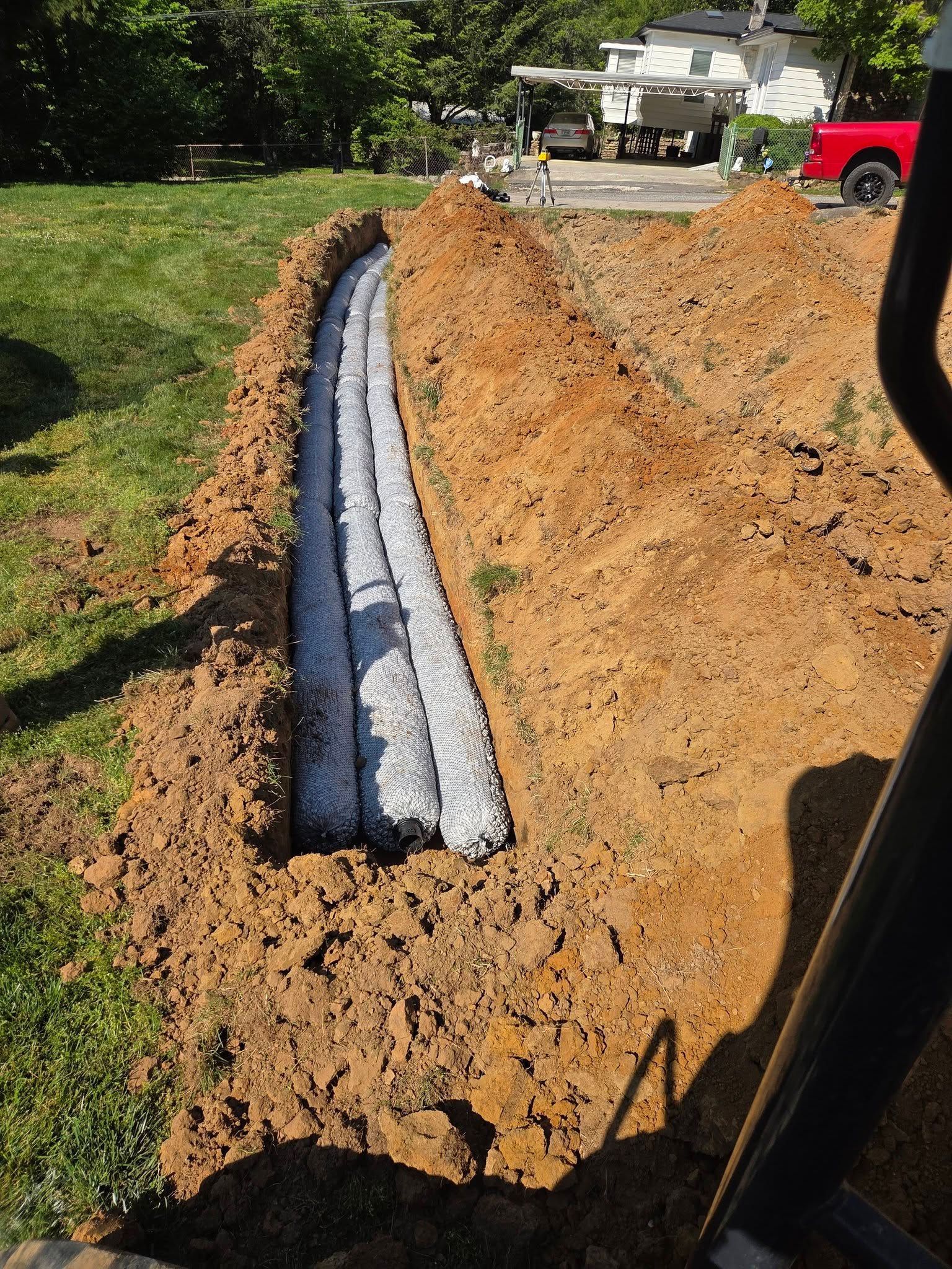 Trenched yard with drainage pipe and gravel bed beside a dug dirt embankment under construction