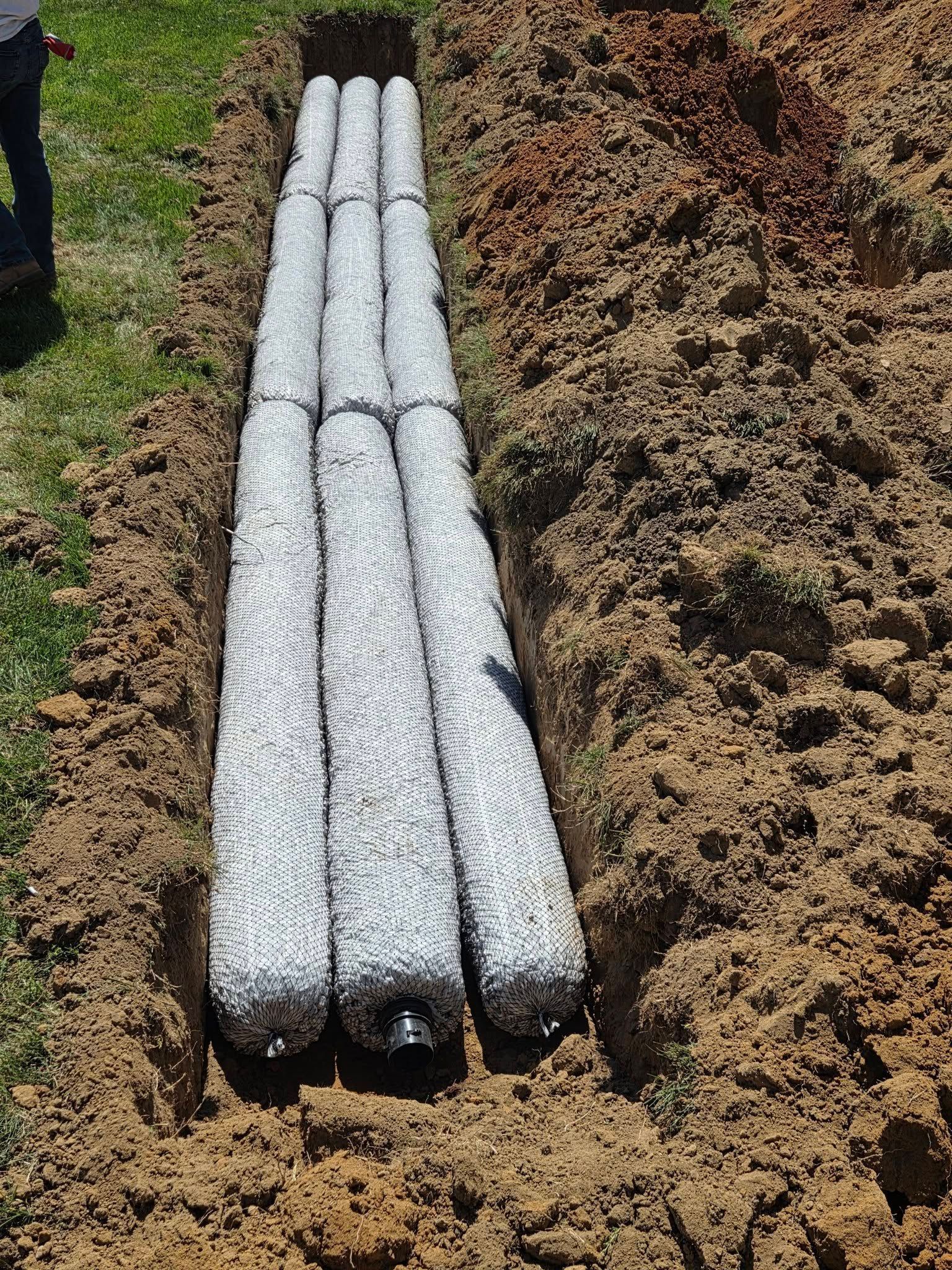 White wrapped bundles laid in a dirt trench between garden rows