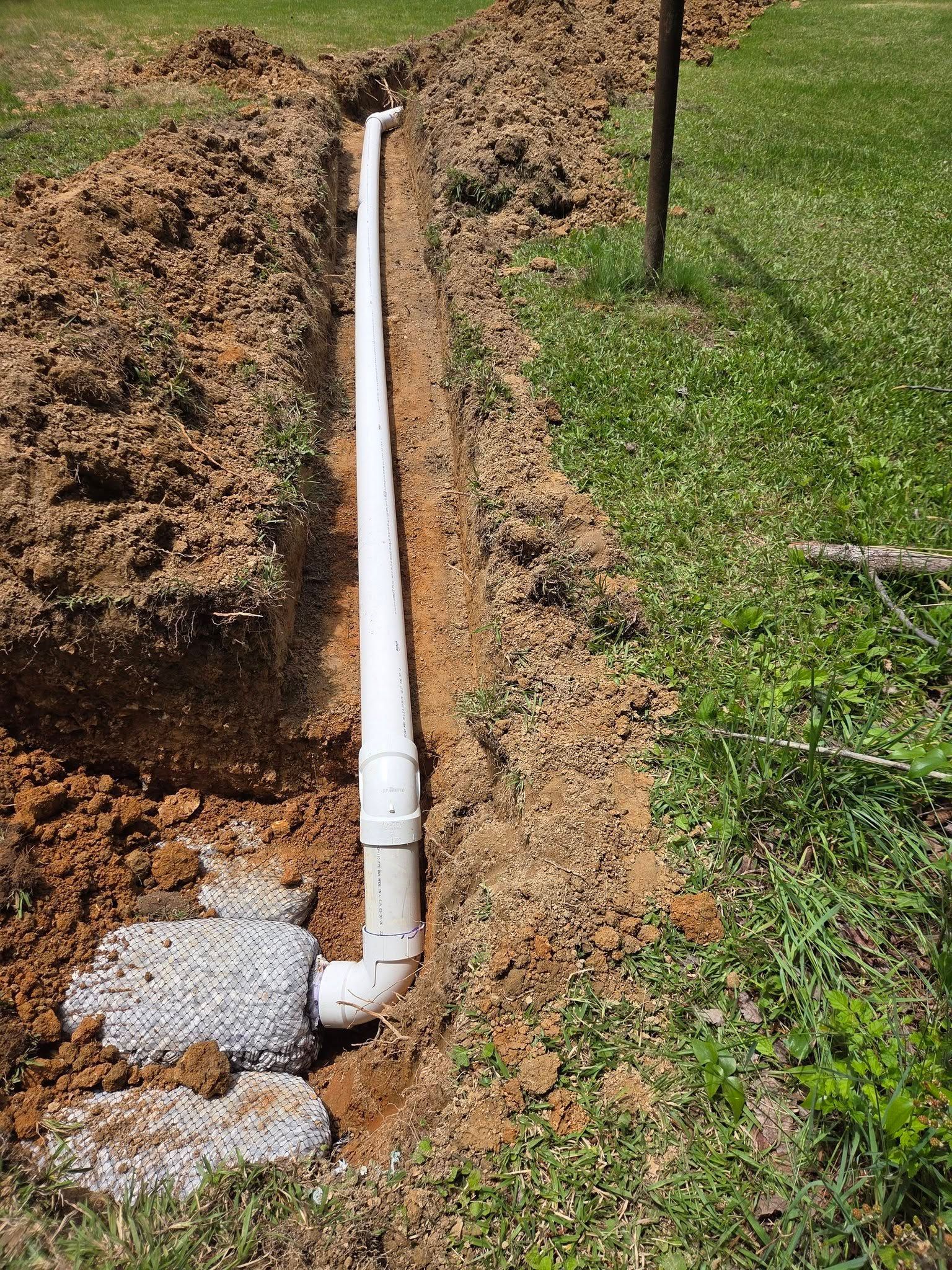 White PVC pipe trench in a dirt yard beside green grass and a utility post.
