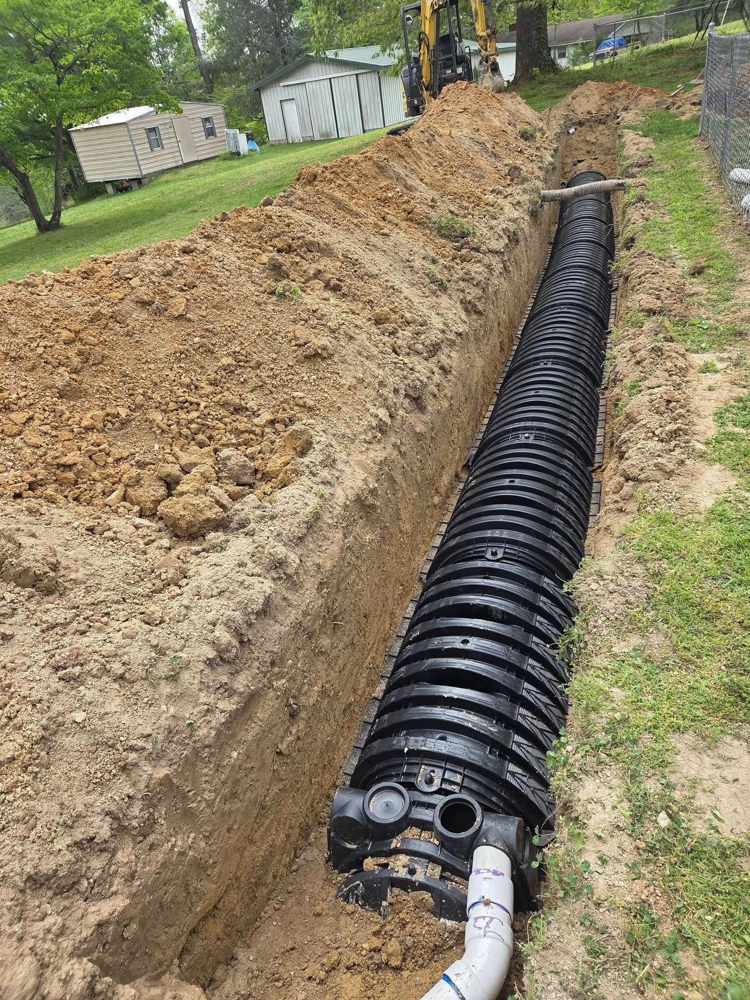 Black drainage pipe laid in a trench beside a dirt embankment, with white pipe connected at the end.