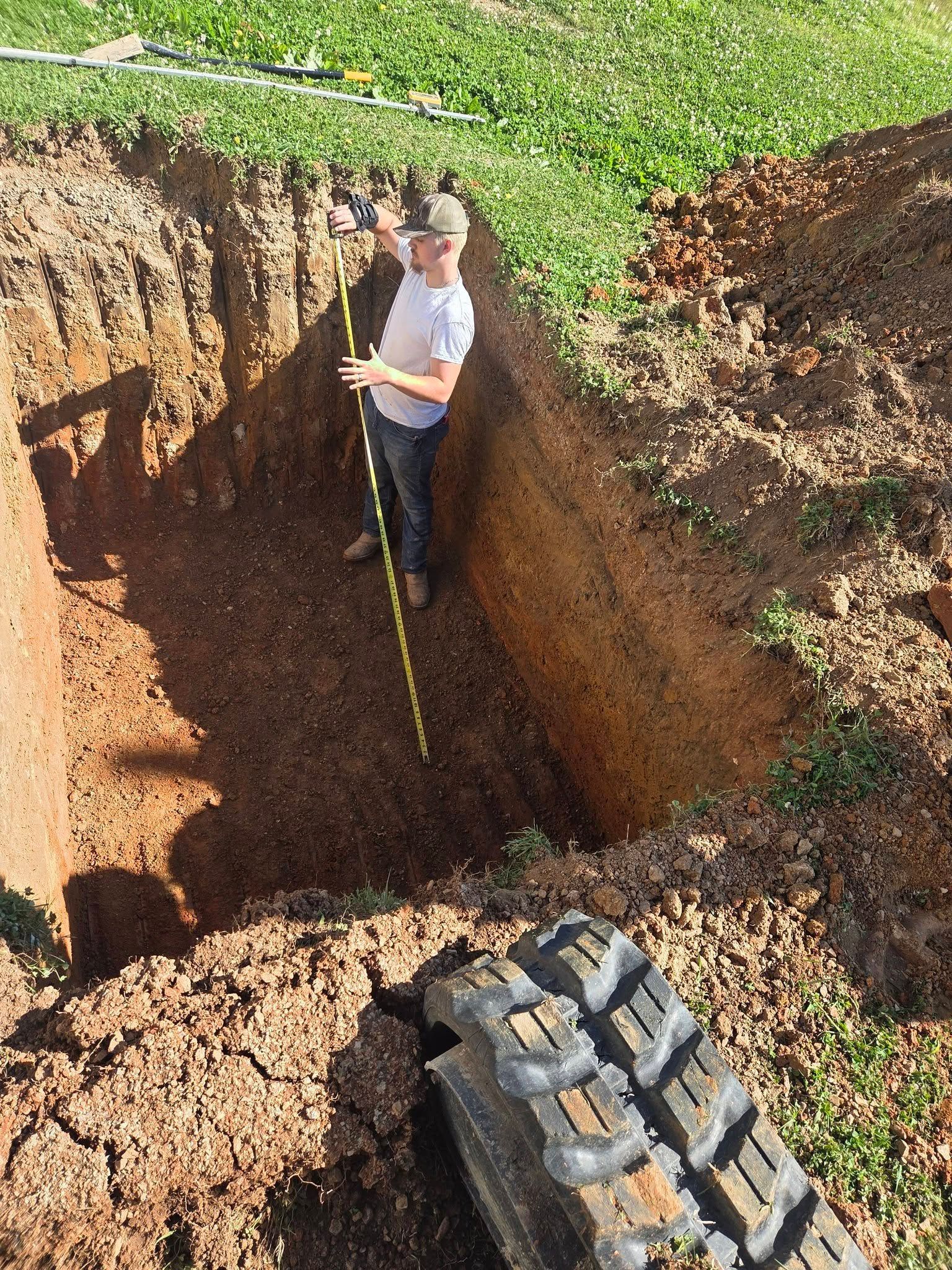 Person measuring the depth of a large excavation beside a tractor tire in a grassy field