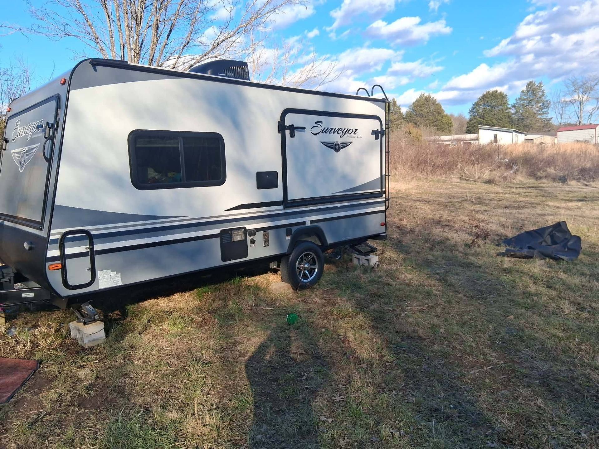 White travel trailer parked on a grassy lot beside trees under a clear sky.