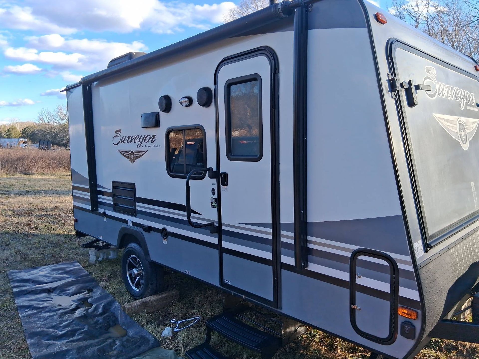 White and gray travel trailer with black trim parked outdoors on grass under a blue sky
