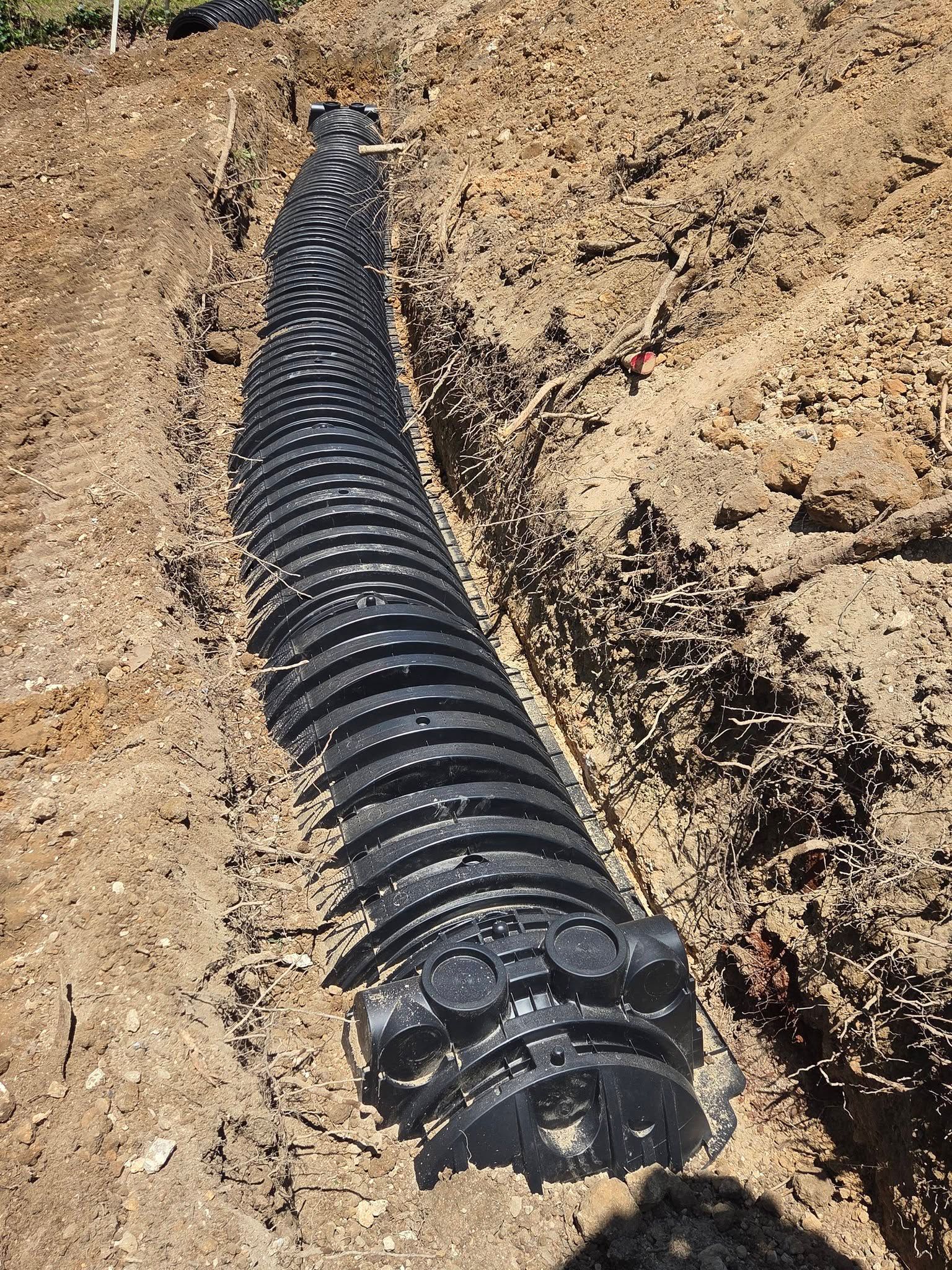 Black corrugated pipe laid in a dirt trench at a construction site.