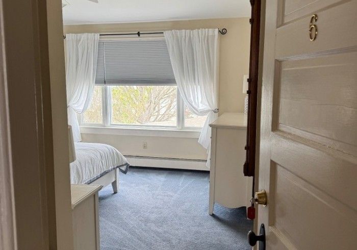 The door is open to a bedroom with a bed and a window.