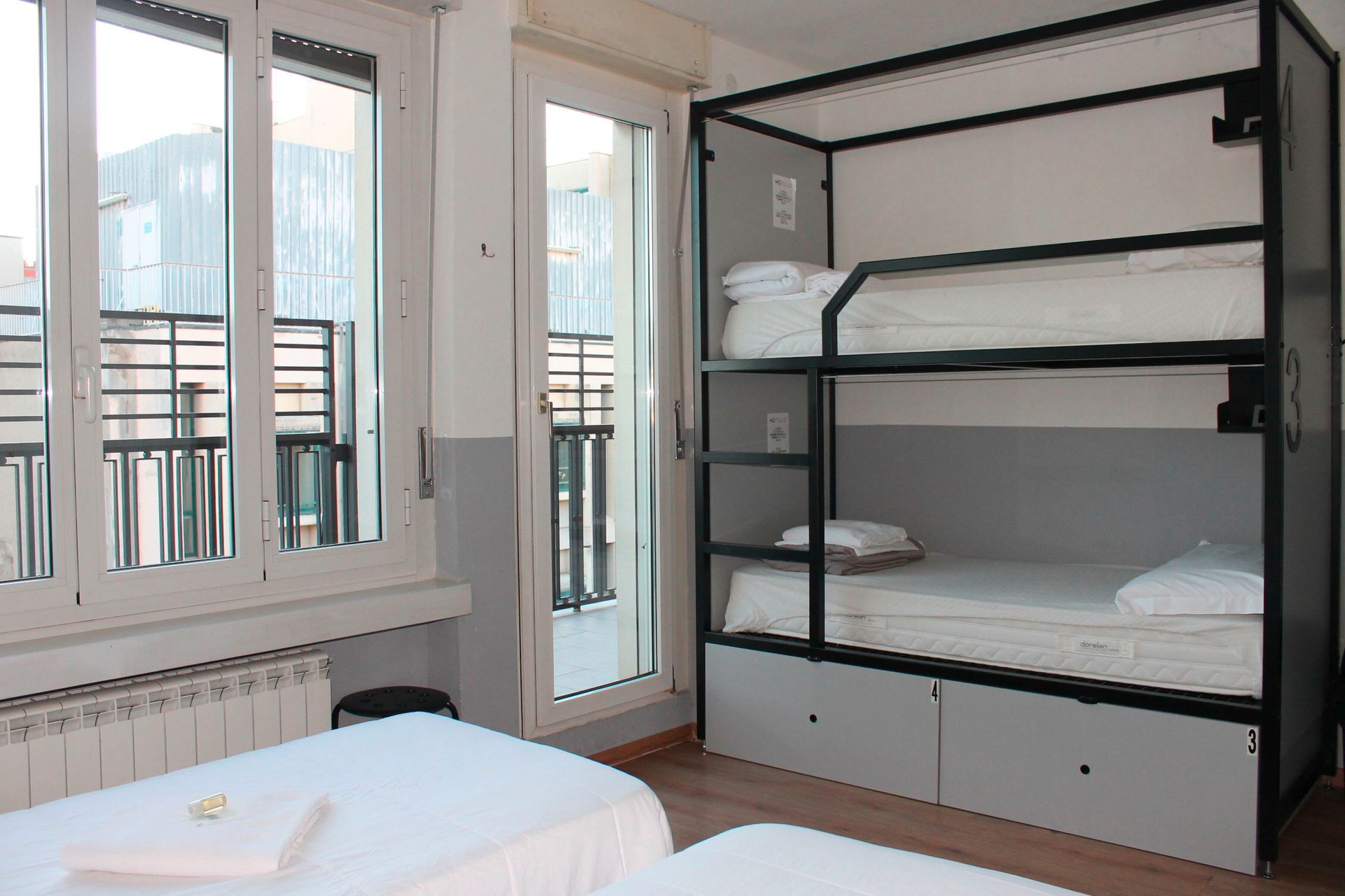 Letti a castello e un letto singolo in una stanza luminosa con ampie finestre e un piccolo balcone.